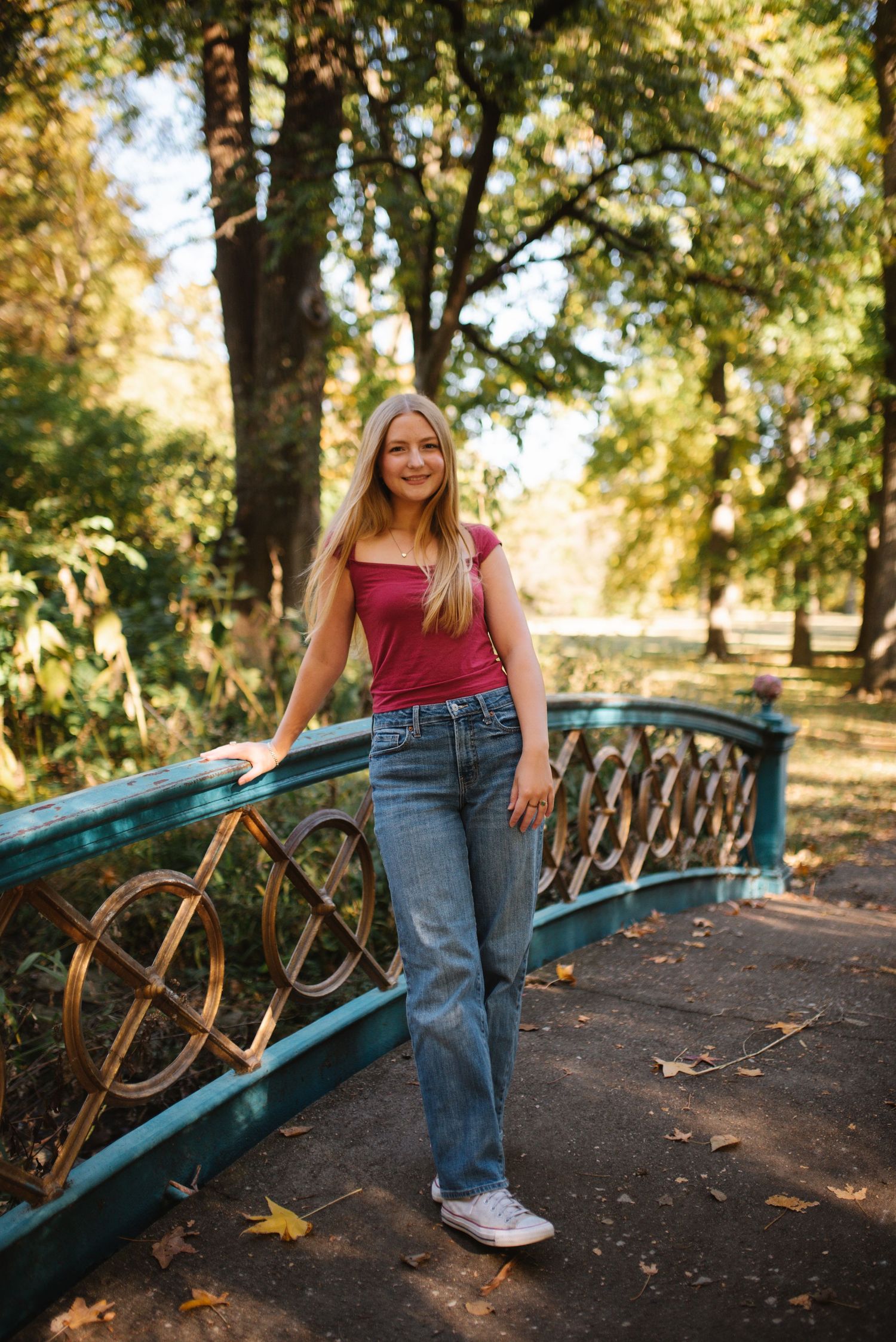 A person in a yellow cardigan and jeans walks along a stone path in a sunlit garden with trees and greenery.