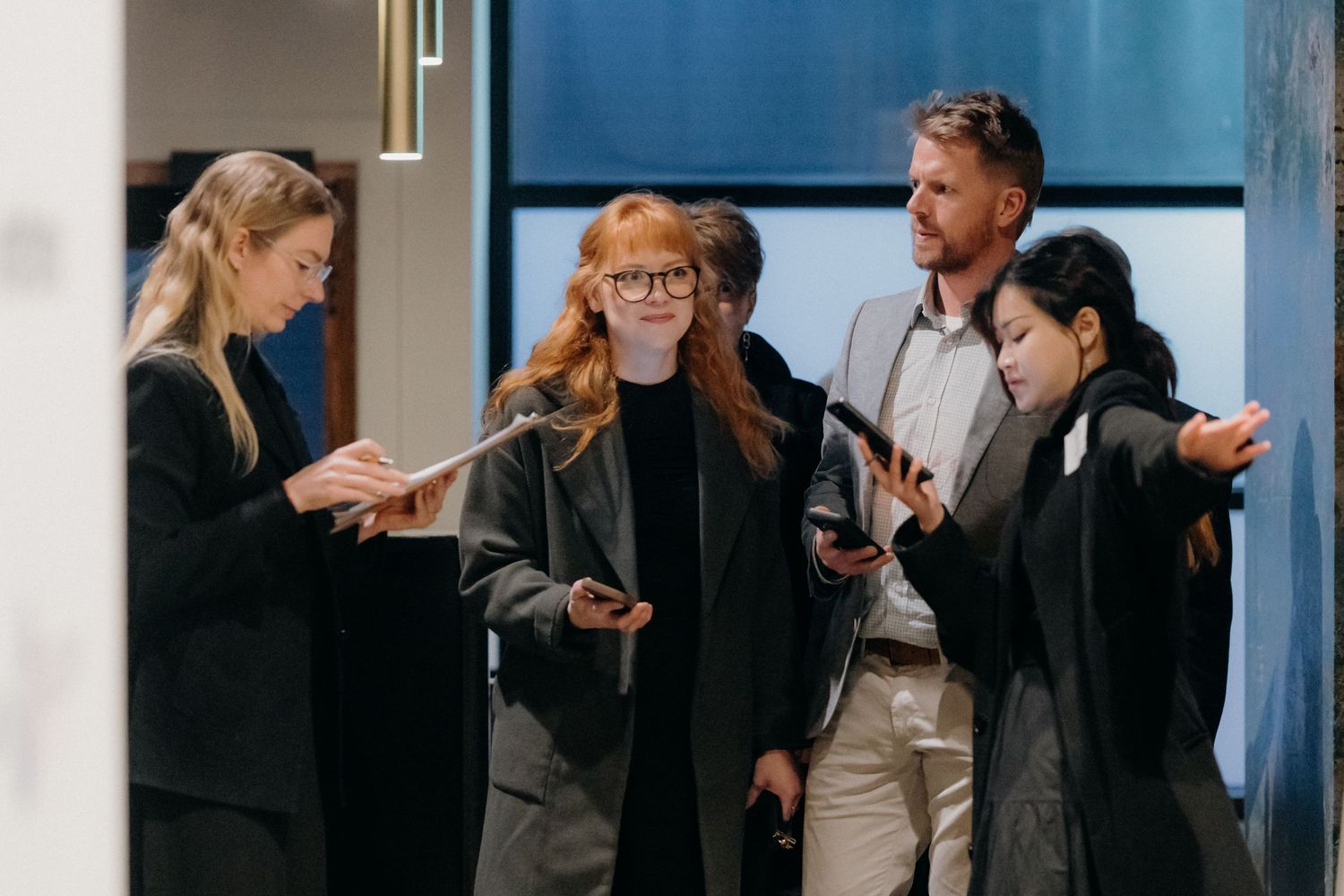 Four business professionals reviewing documents and smartphones in a modern office corridor.
