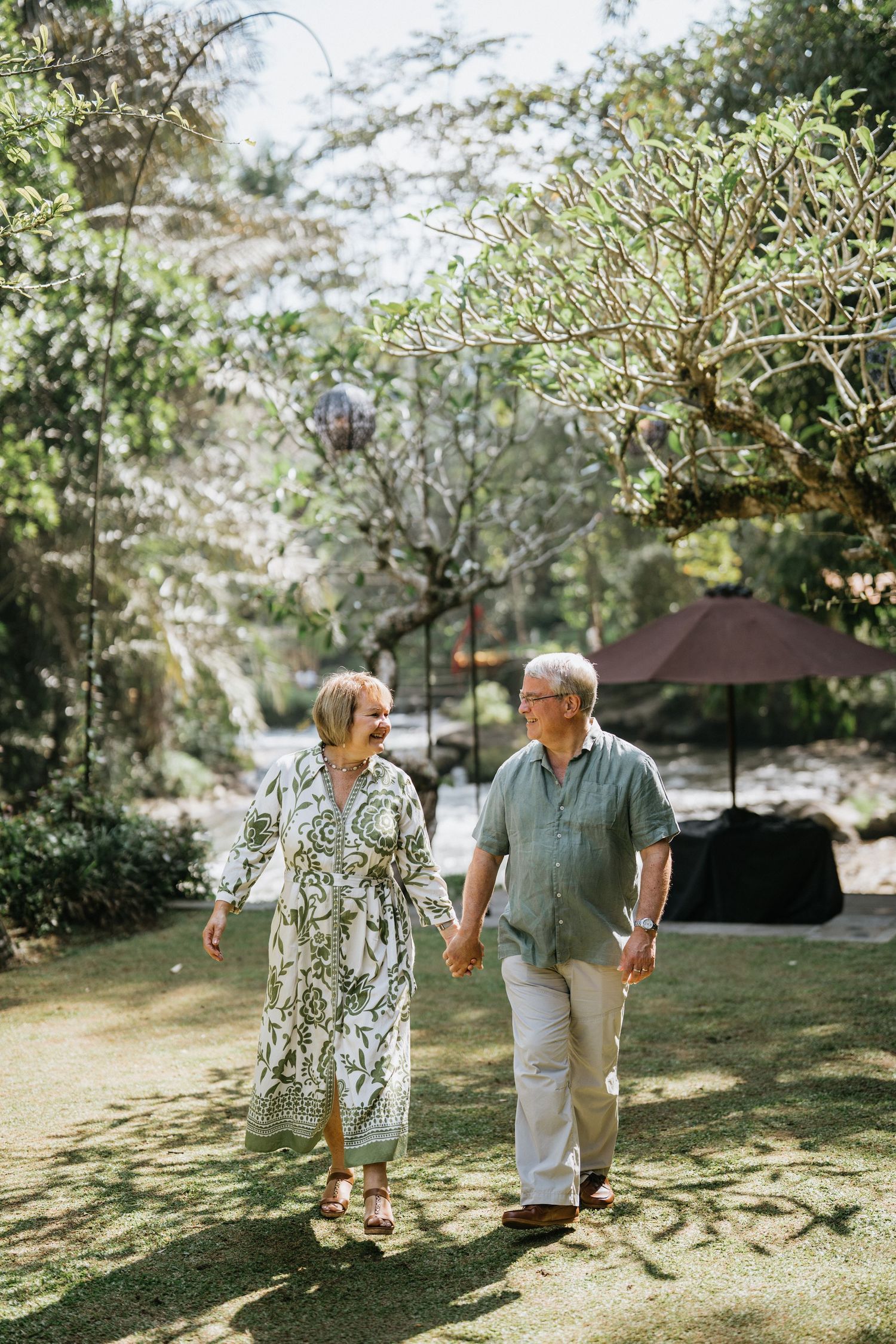 Couple walking along a green garden pathway surrounded by tropical plants.