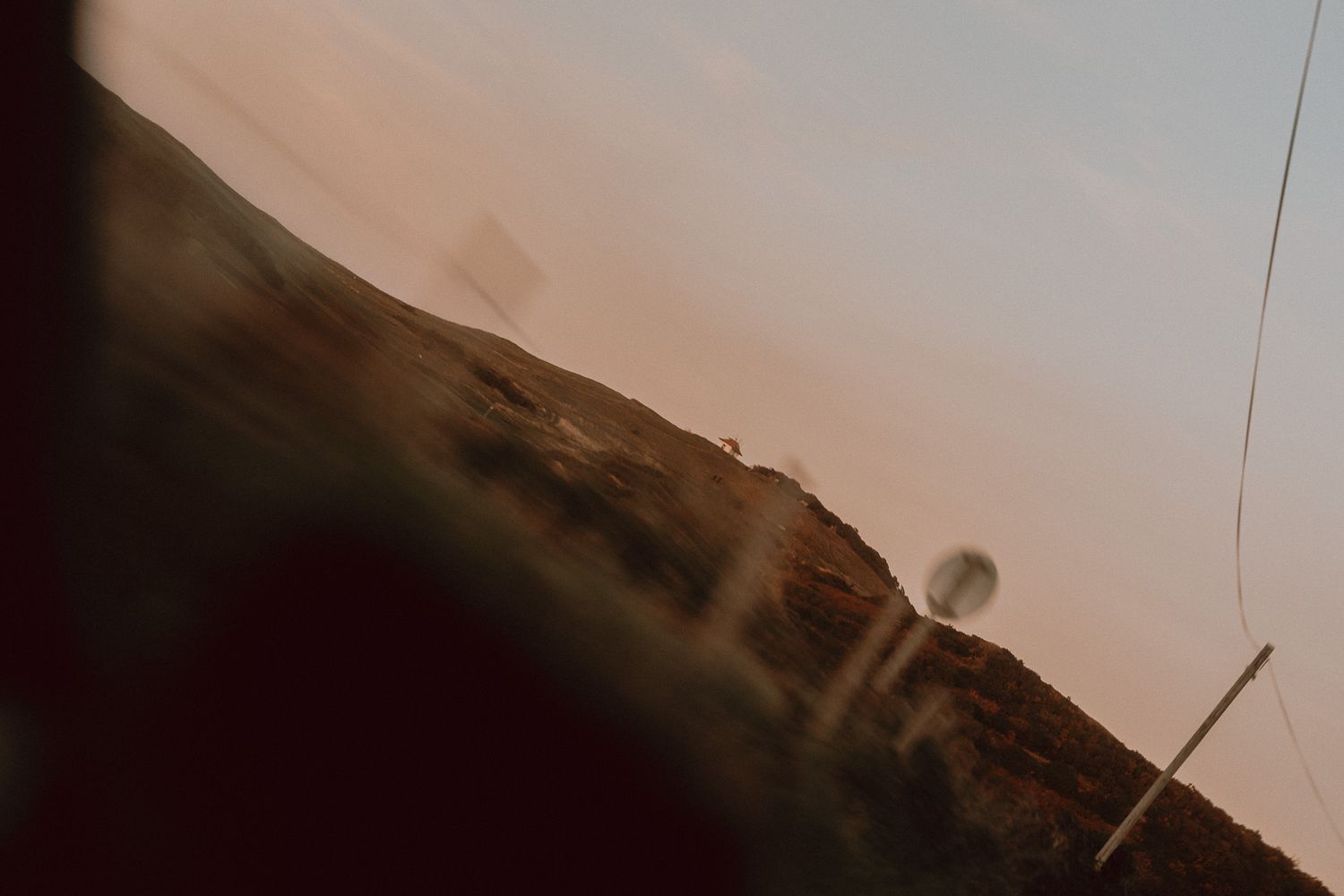 Blurred view of a hilly coastal landscape in Sheringham, Norfolk, at dusk with a warm pink sky and rocky terrain, taken from a moving car.