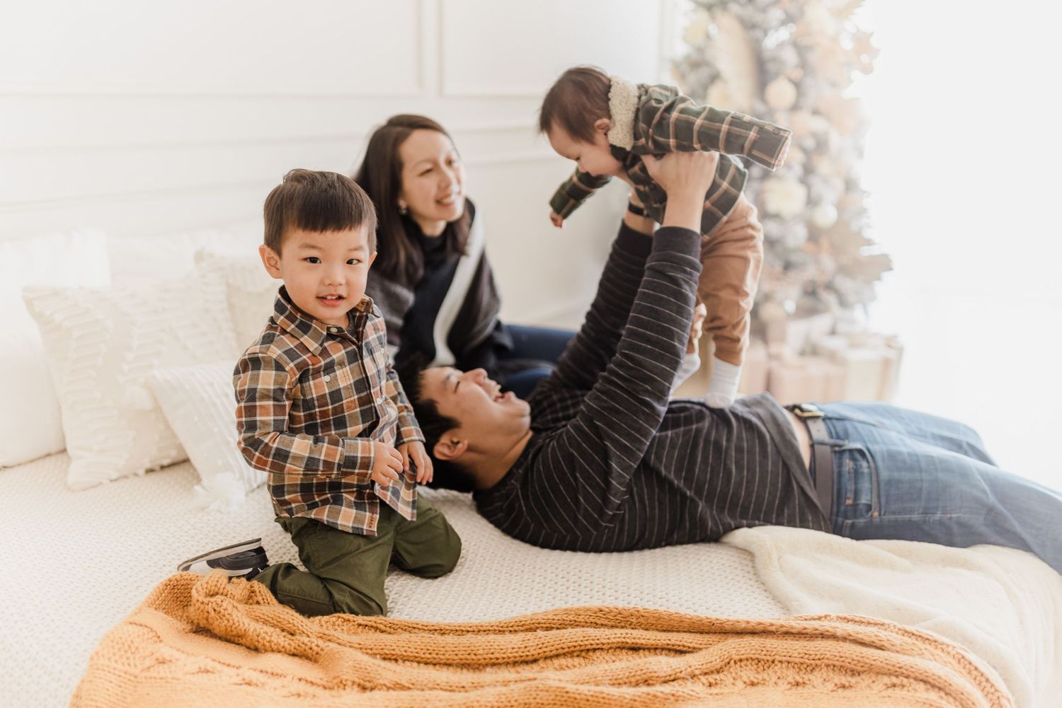 Playful family moment on a cozy blanket with Christmas tree in the background.