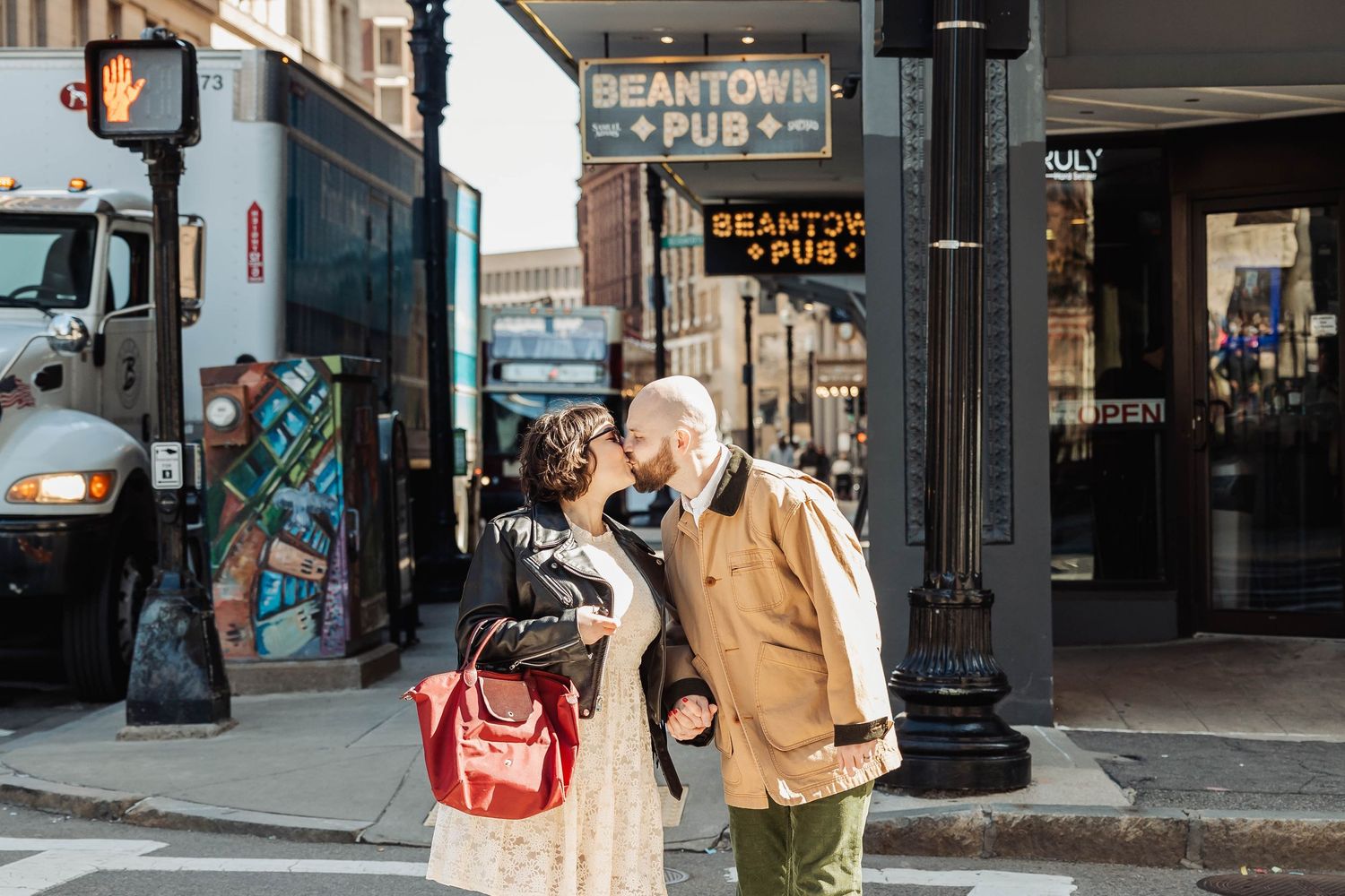 Two people stand near a Beantown Pub sign on a city street corner.