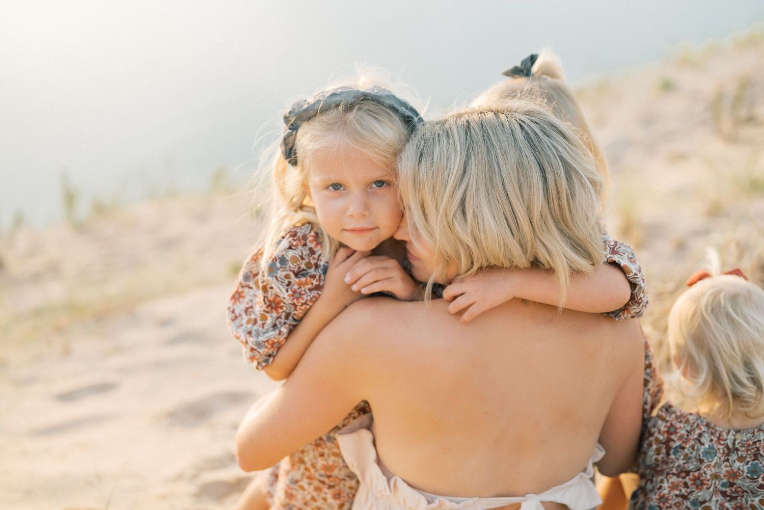 Children embracing a person in a heartfelt outdoor moment at sunset.