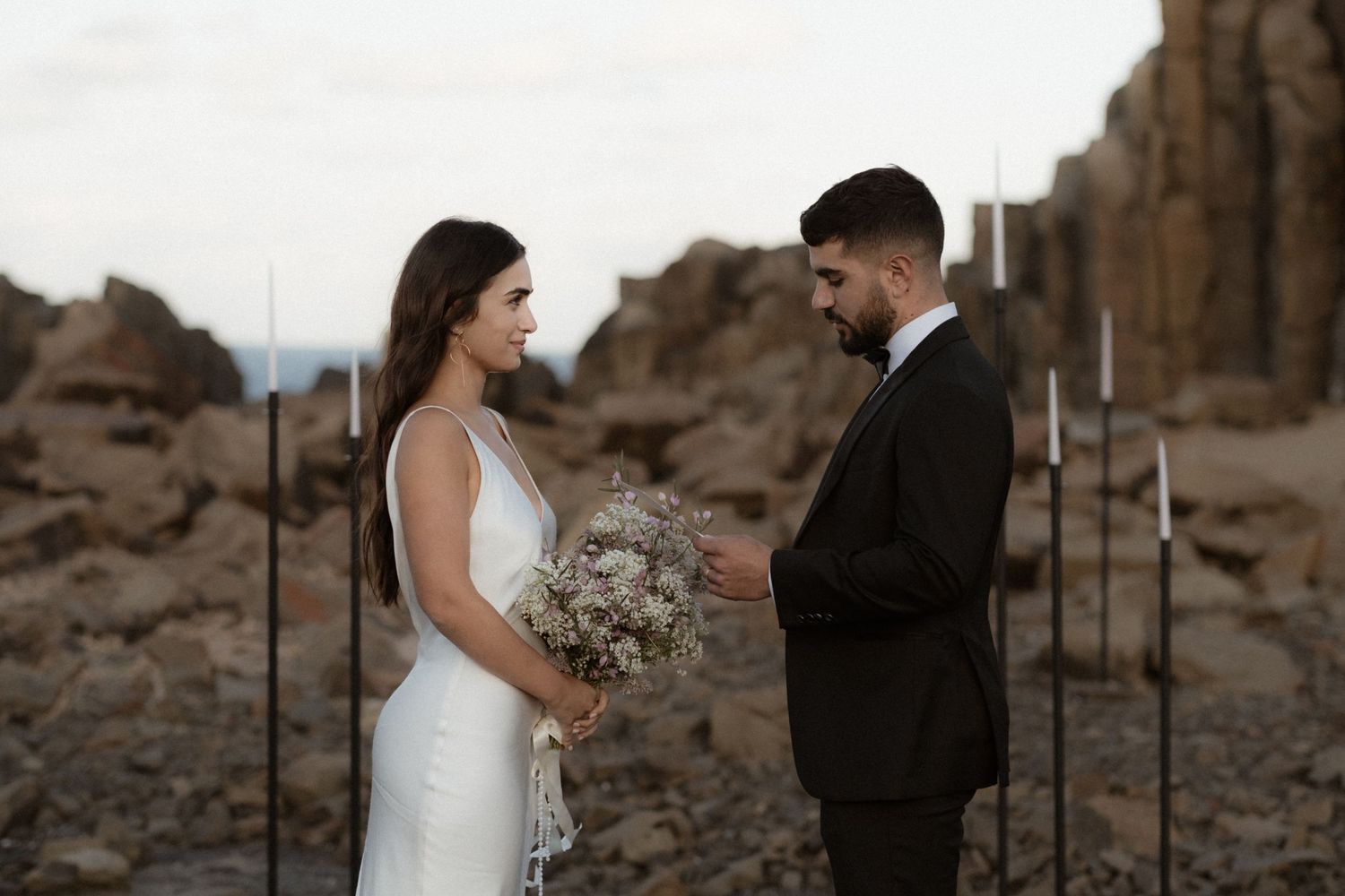 Couple exchanging vows against rocky desert backdrop with dried flower bouquet.