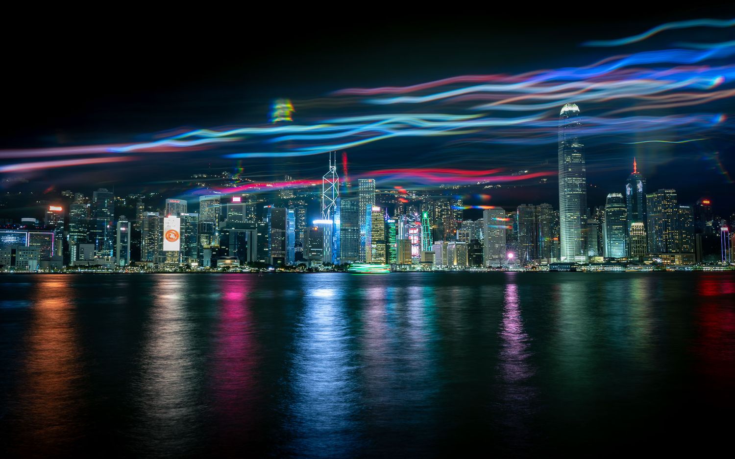 Vibrant Hong Kong skyline at night with colorful light trails reflecting on the harbor waters.