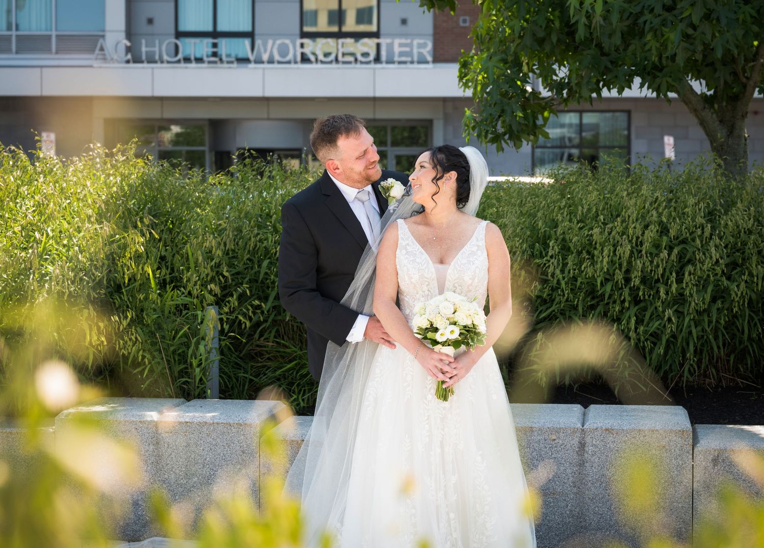 A bride and groom share a romantic kiss outside Hotel Worcester surrounded by lush greenery on their wedding day.