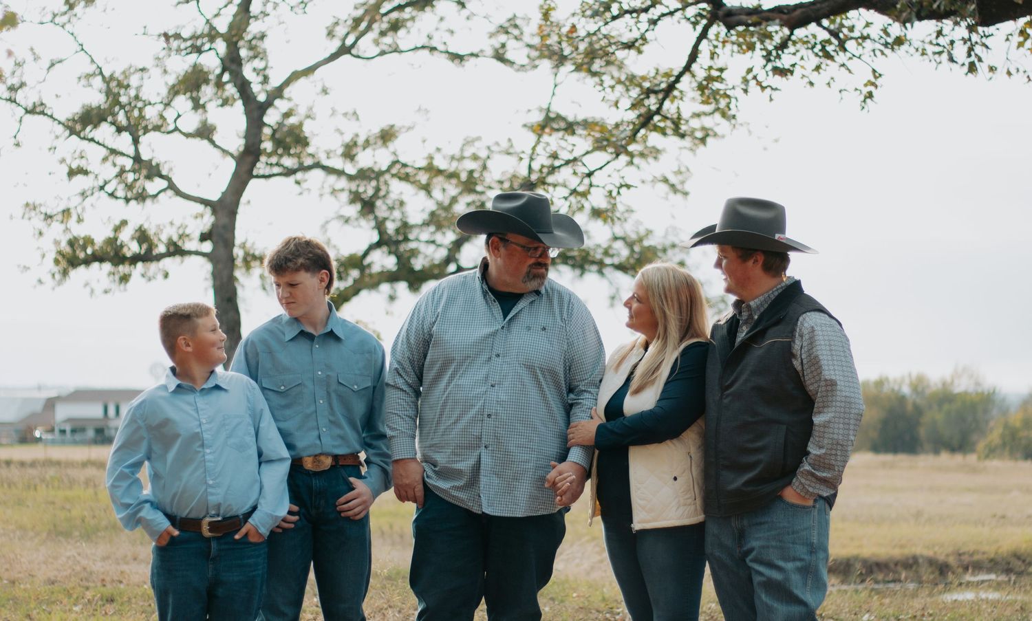 Group of ranchers in denim and cowboy hats standing together in a field during autumn.