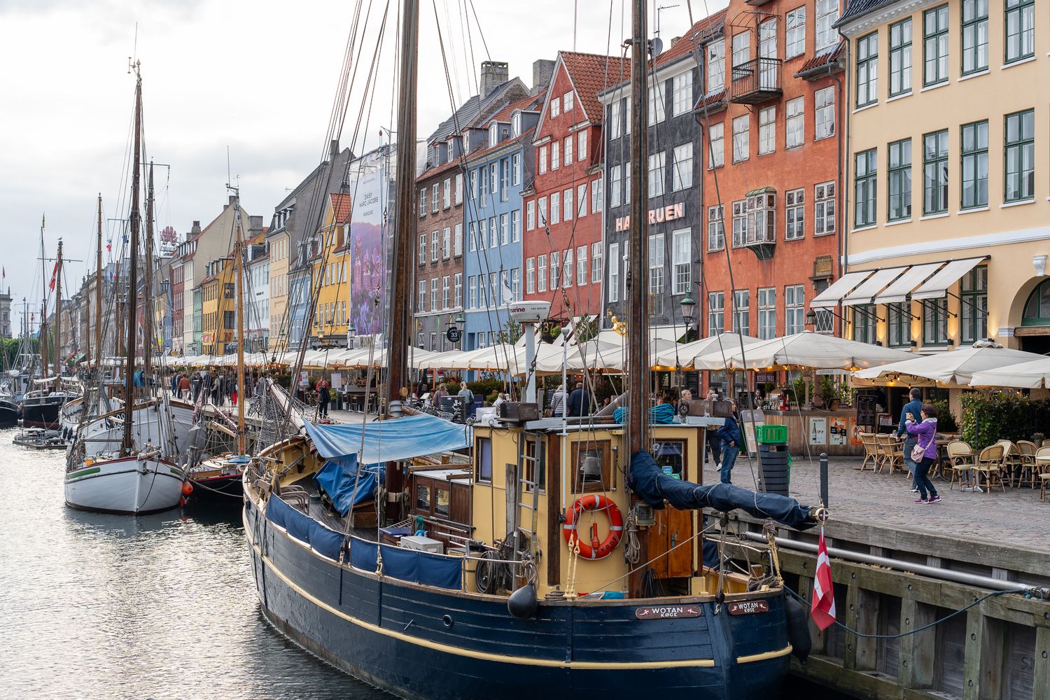 Colorful historic buildings line the waterfront at Nyhavn harbor in Copenhagen with boats docked along the canal.