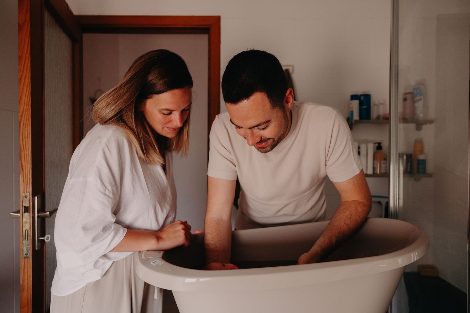 Parents smiling together while bathing their newborn baby in a small tub.