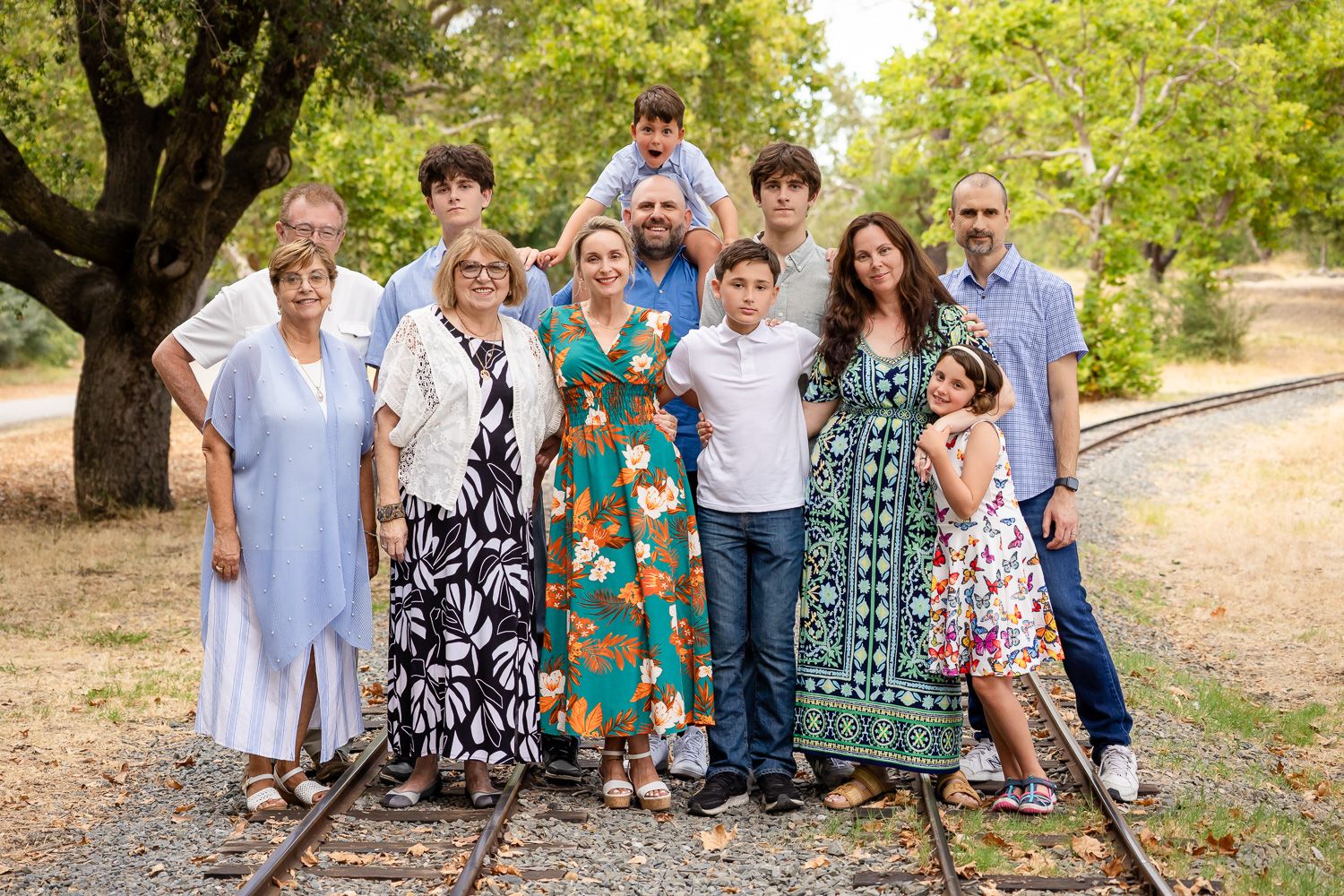 Multi-generational family posing together on railroad tracks surrounded by trees during an outdoor photo session in Los Gatos