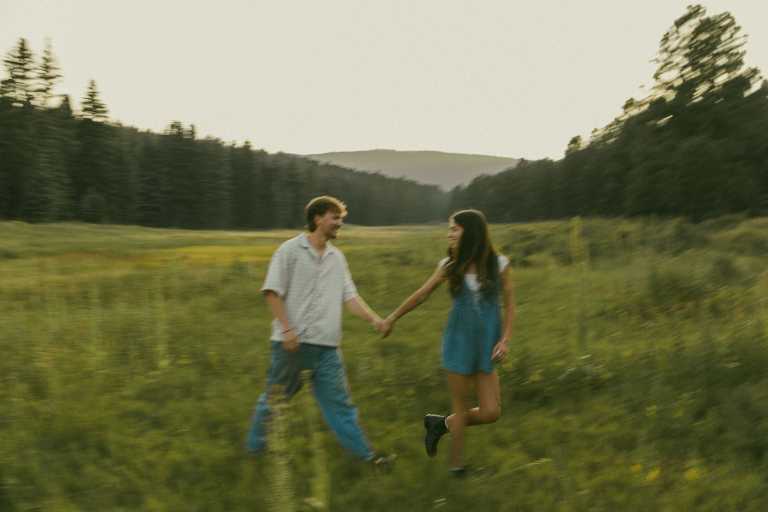 Couple walking hand in hand through a scenic mountain meadow at sunset.