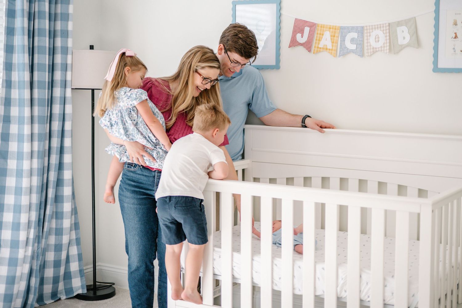 Parents and toddler lean over a white crib in a blue baby nursery named Jacob.