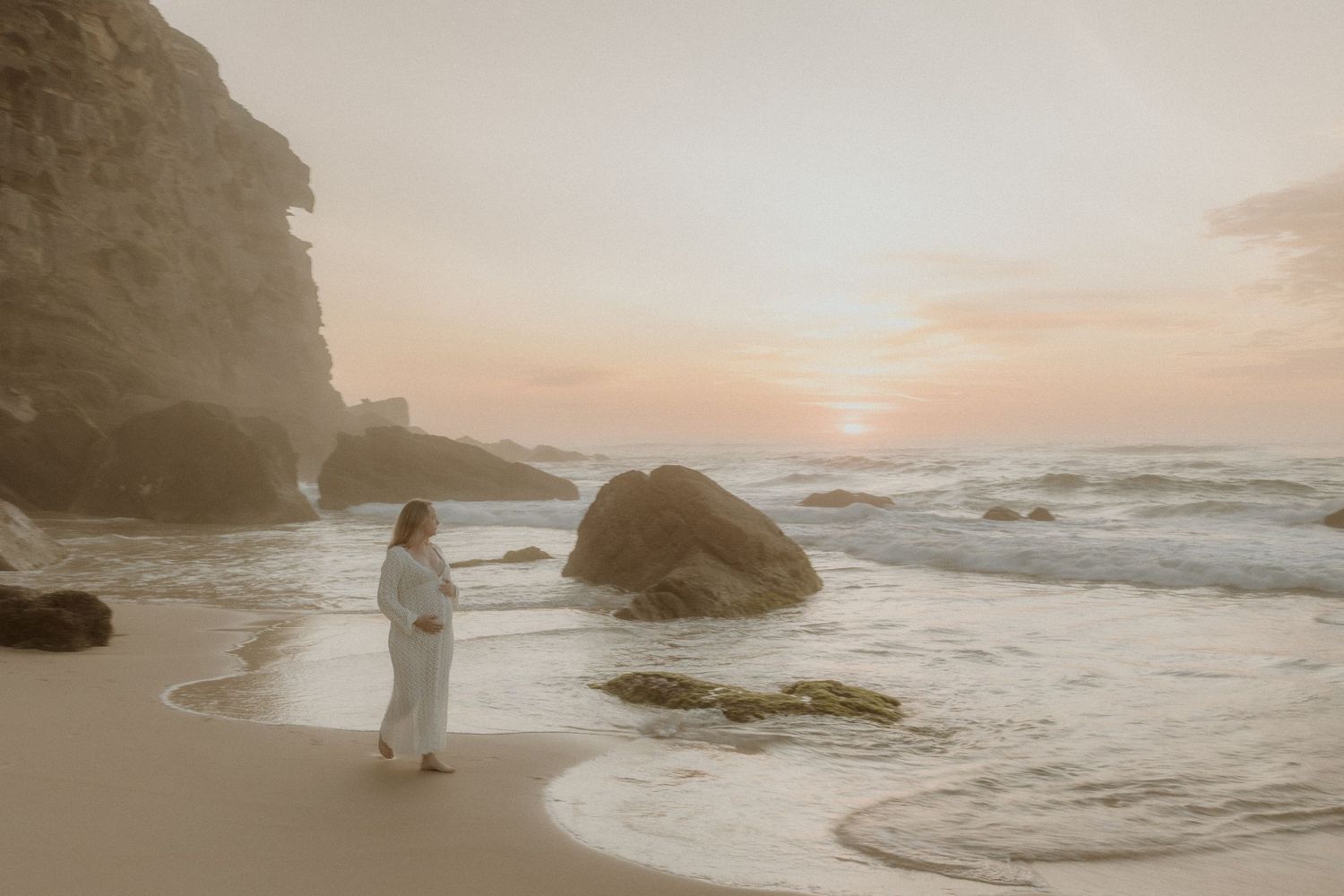 A dreamy coastal engagement session shows a couple walking along a misty beach at sunset with crashing waves.