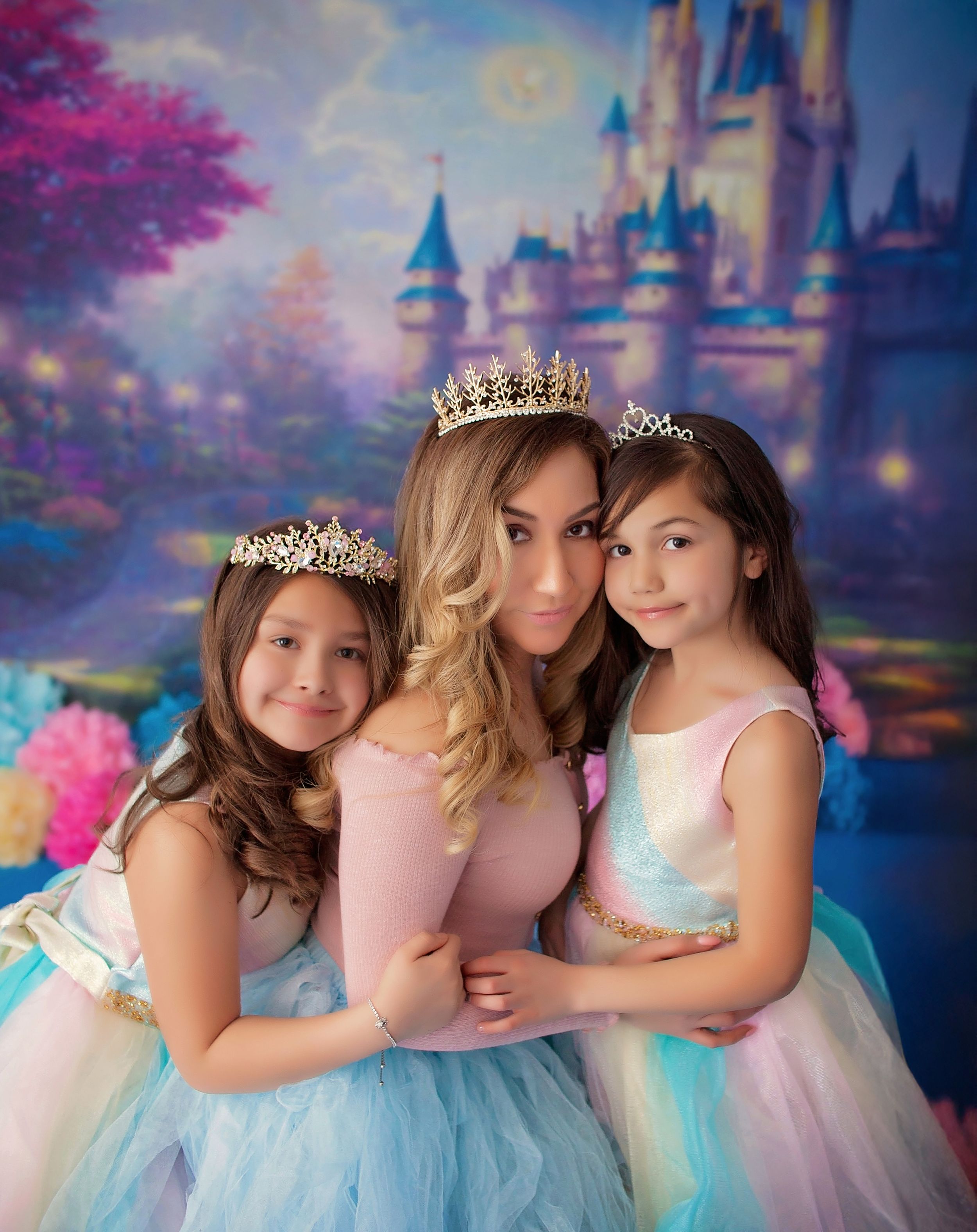 A group in pastel princess dresses and tiaras pose together against a dreamy castle backdrop with pink cherry blossoms.