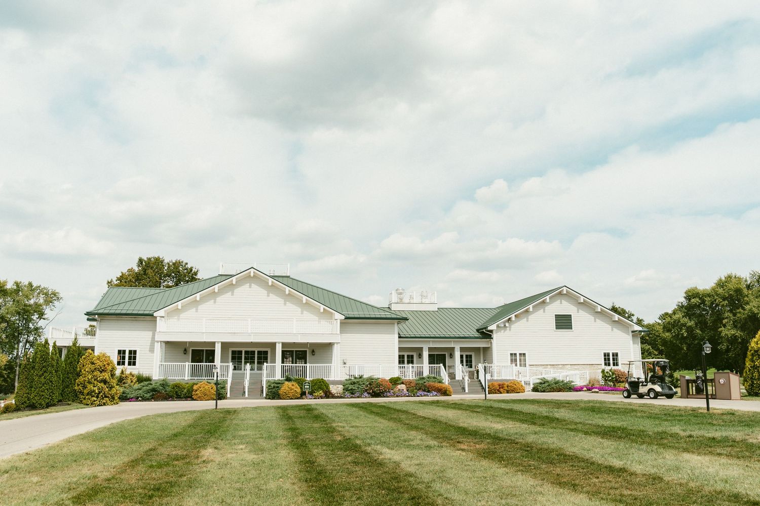 Panoramic view of white ranch-style Sugar Valley Golf Club on a grassy hillside under cloudy skies. Located in Bellbrook, Ohio.