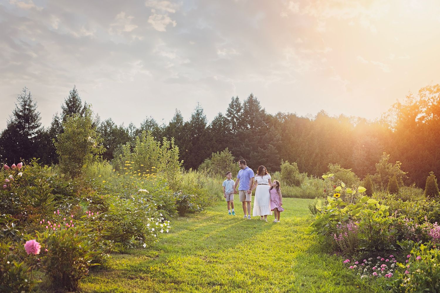 A garden path through blooming flowers and trees at golden sunset with figures walking in the distance.