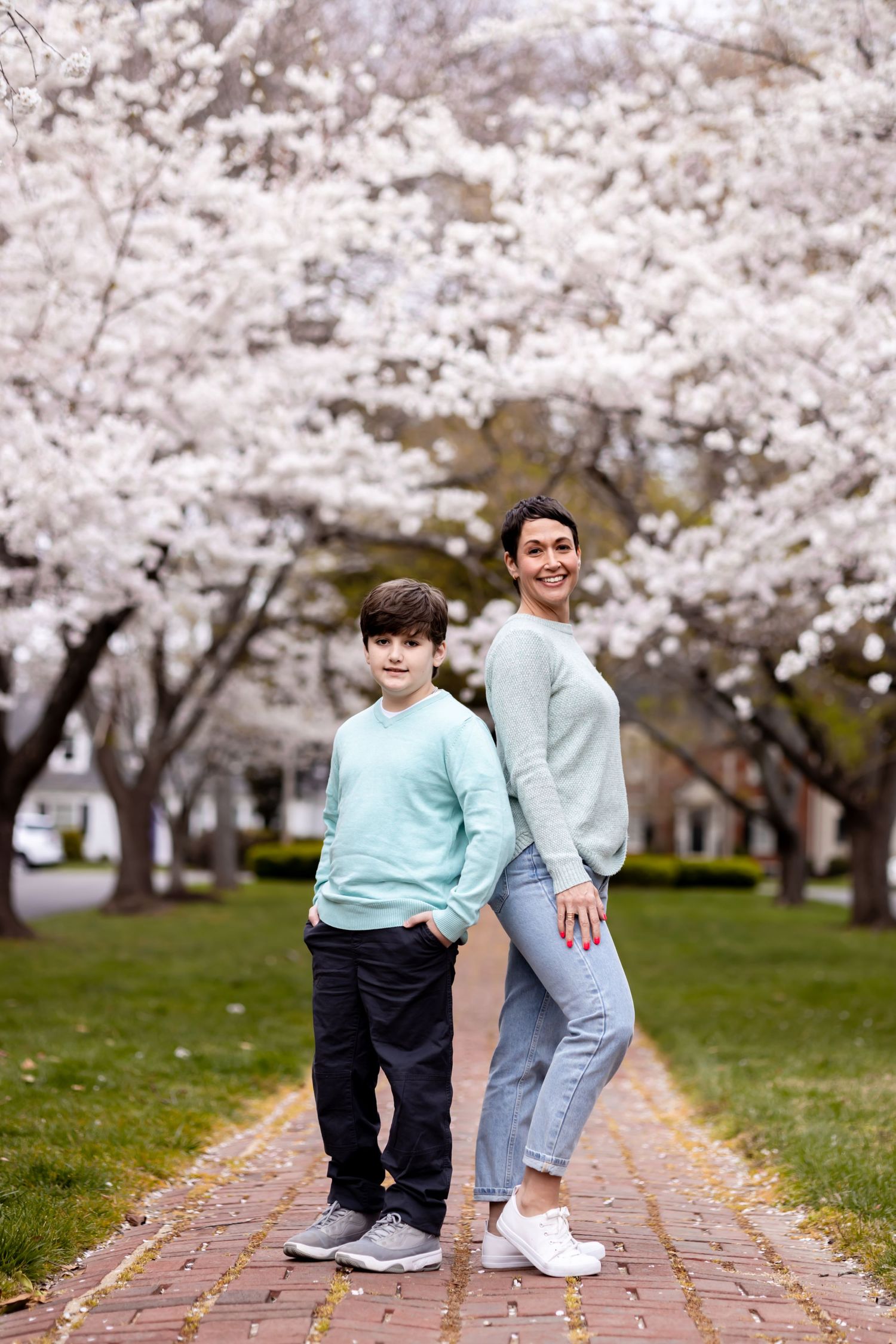 Family standing on brick path under blooming cherry blossom trees wearing matching blue sweaters.