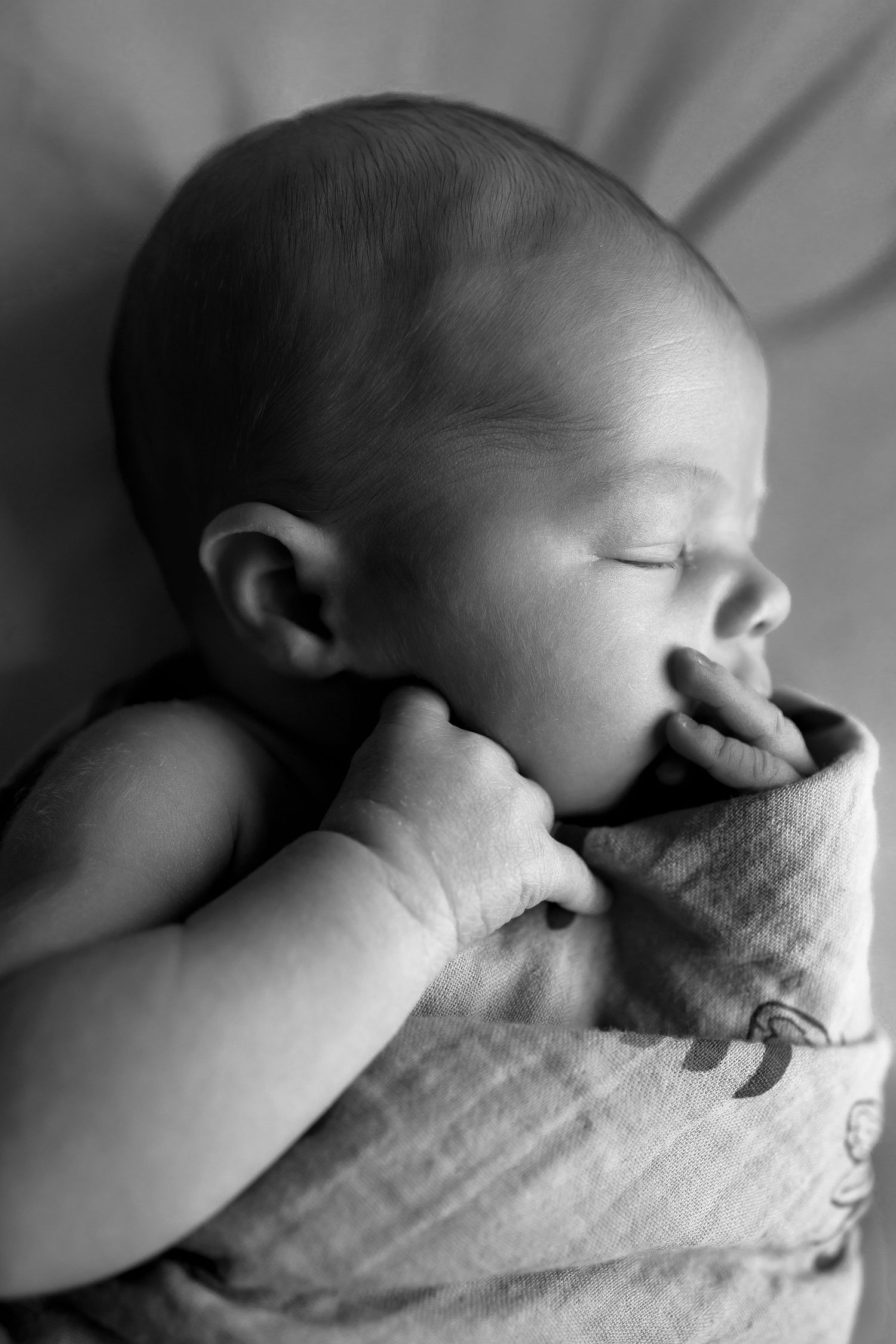 Close up black and white shot of a newborn with their eyes closed and hand in their mouth