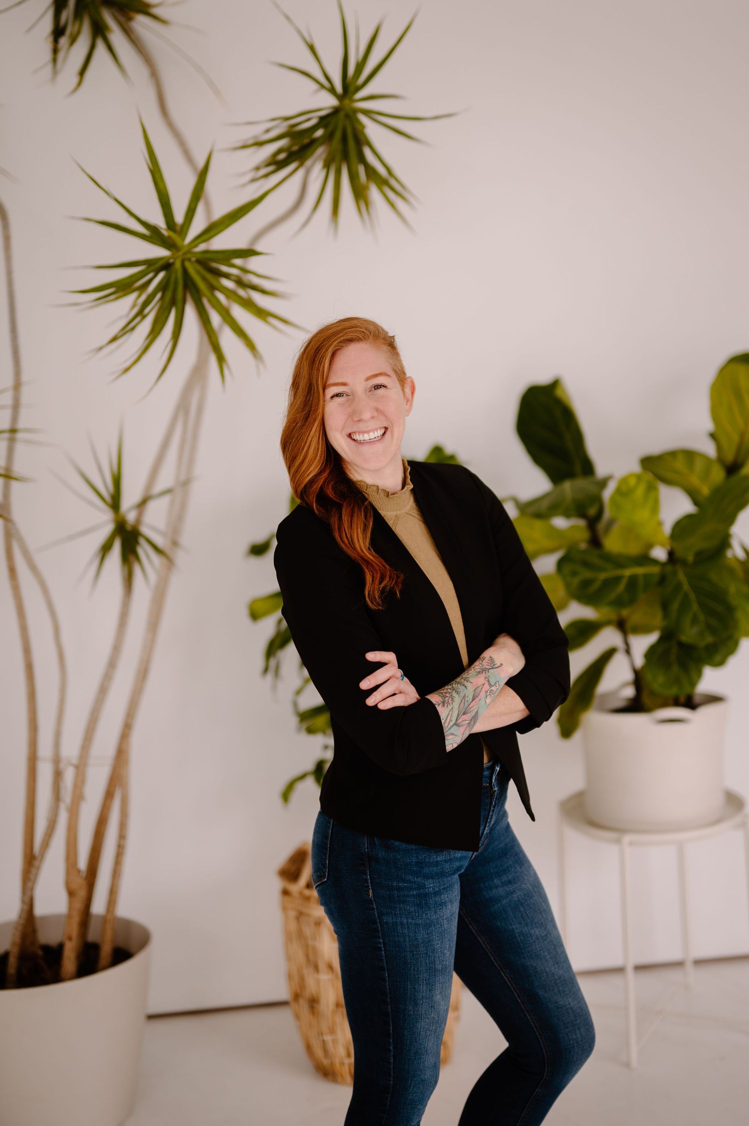 Someone poses casually in jeans and black sweater against white wall with decorative air plants and potted foliage.