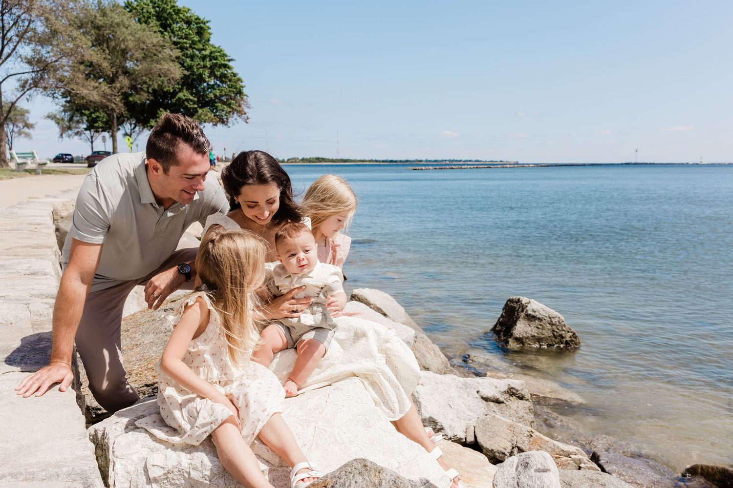 Family relaxing together on rocky shoreline overlooking peaceful lake waters.