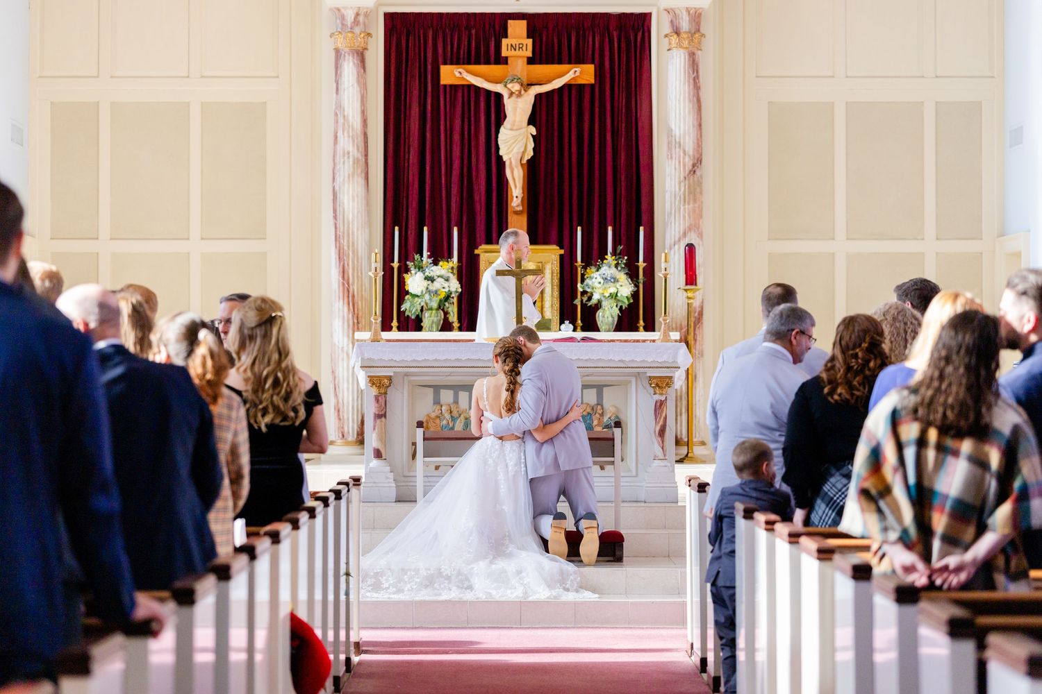An elegant church wedding ceremony taking place with guests seated in pews and a large crucifix mounted above the altar.
