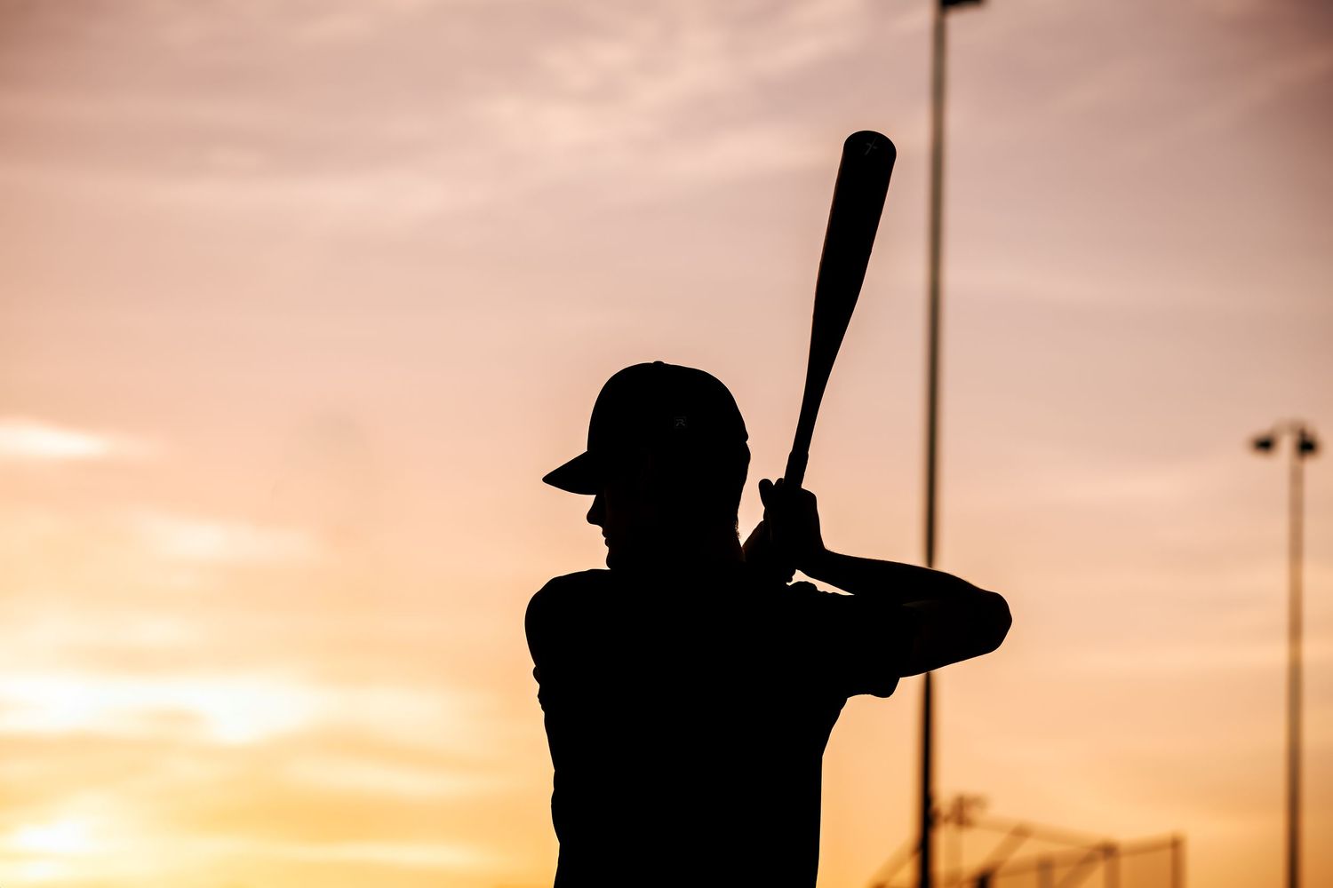 Silhouette of a baseball batter at sunset with warm orange sky in the background.