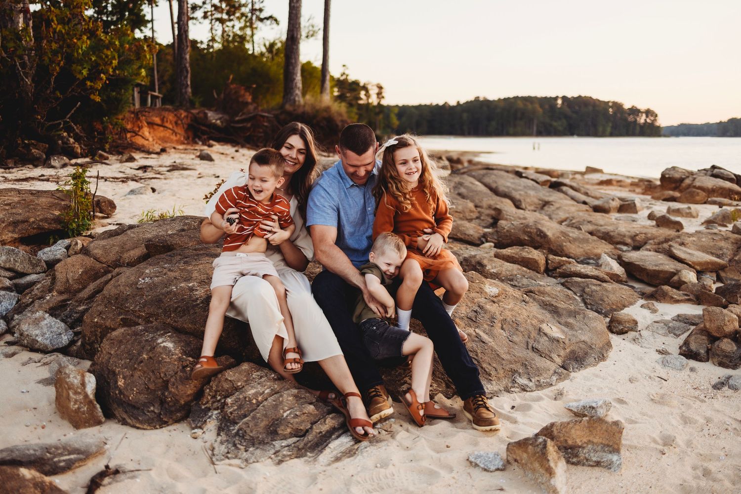 Three people sitting together on coastal rocks at sunset.