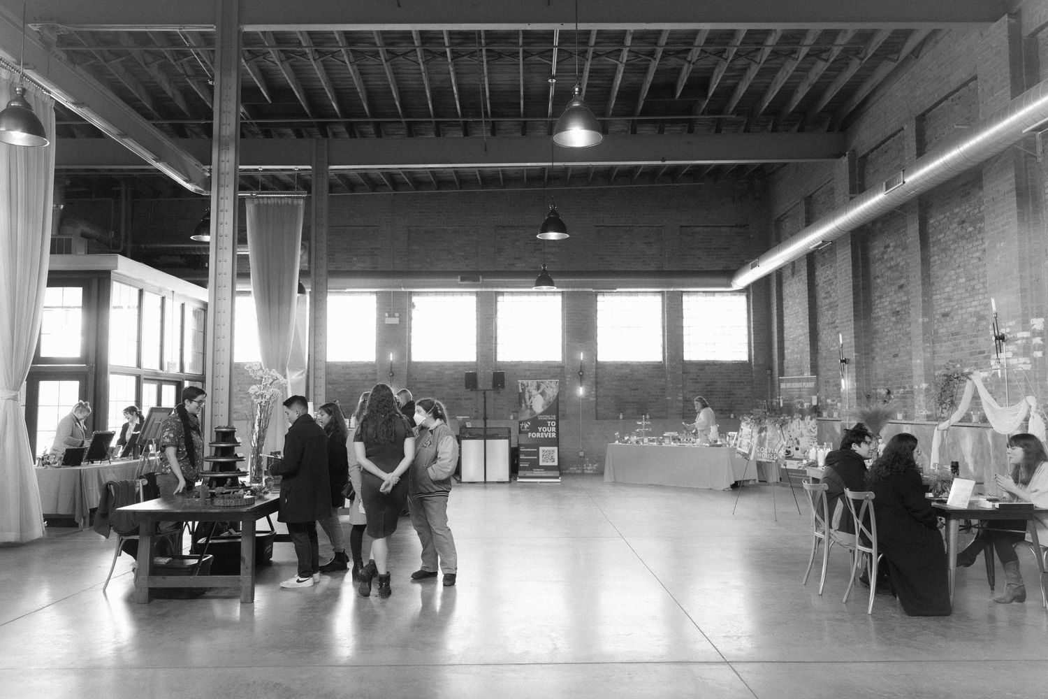Large industrial event space with exposed beams and windows shows guests mingling at tables.