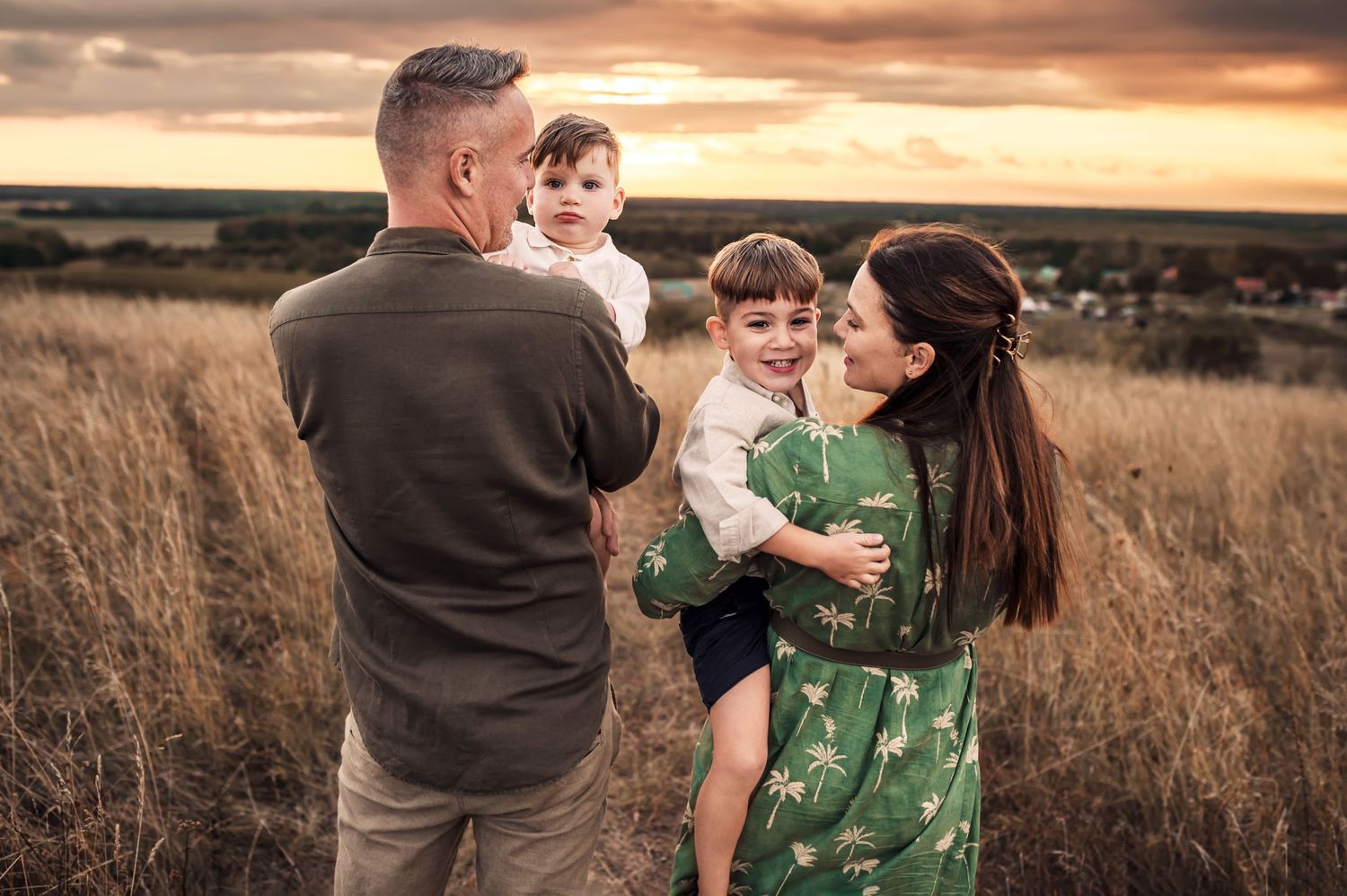 A family shares a tender moment together in a golden field at sunset.