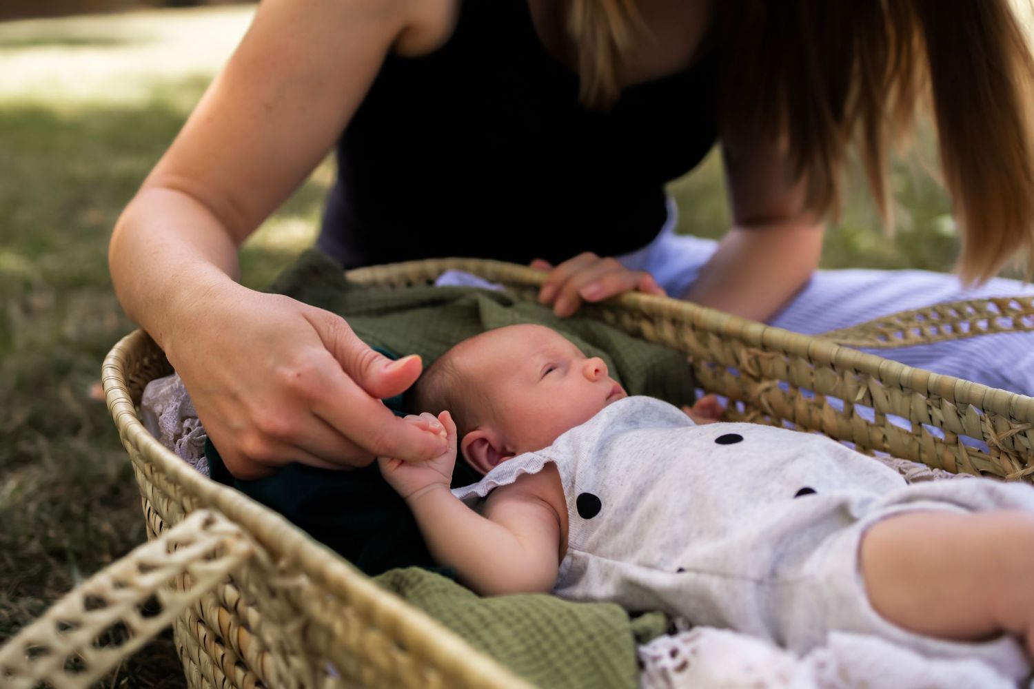 Newborn lying in a basket outdoors while mother gently holds the baby’s hand. Aurora newborn photographer
