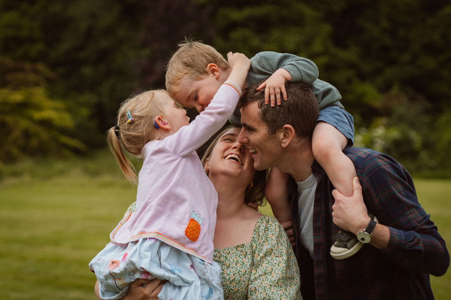A family shares a joyful moment together outdoors on a green lawn with trees in the background.