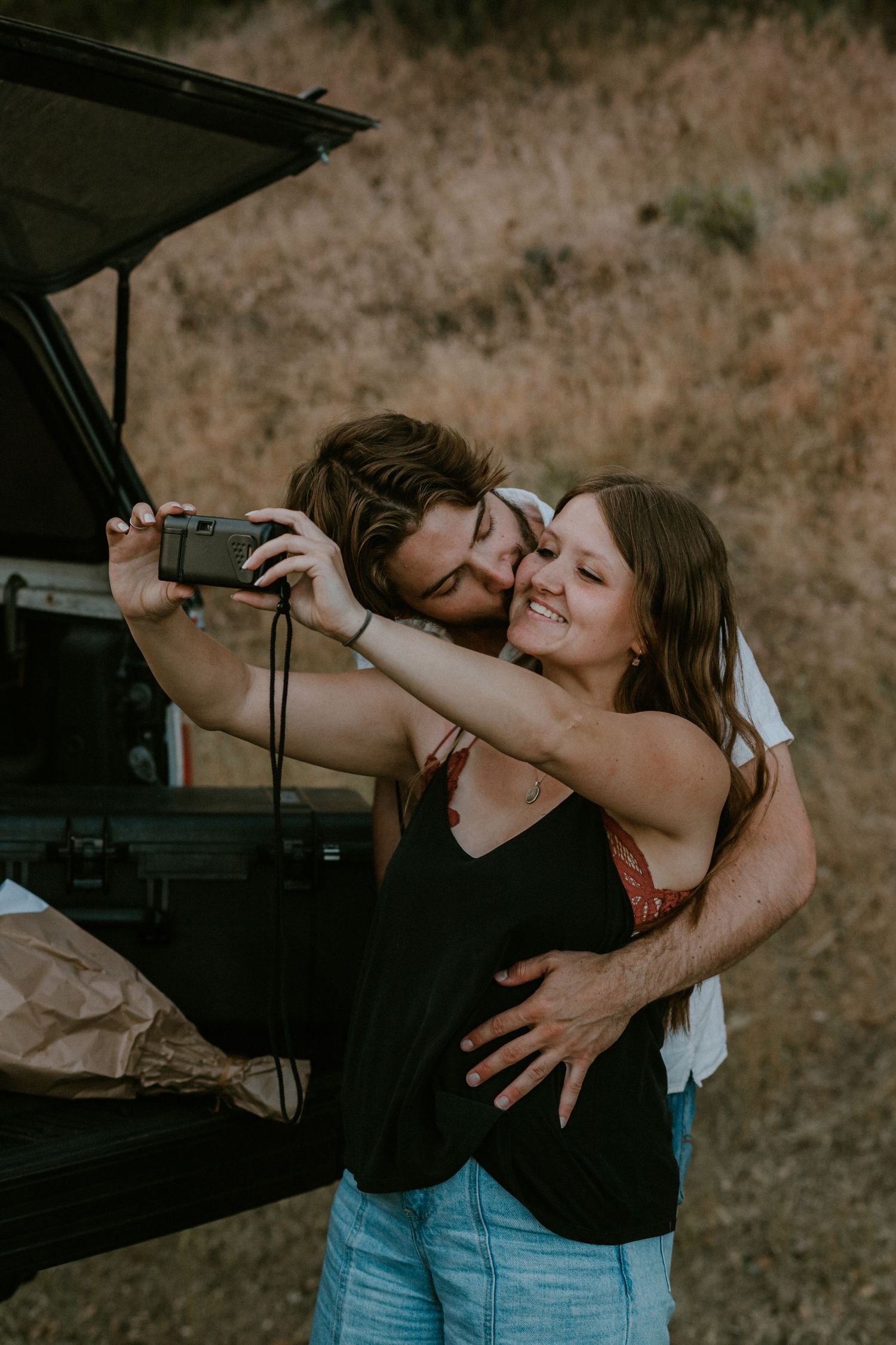 Couple enjoys romantic picnic under a tree on lush green lawn beside white building.