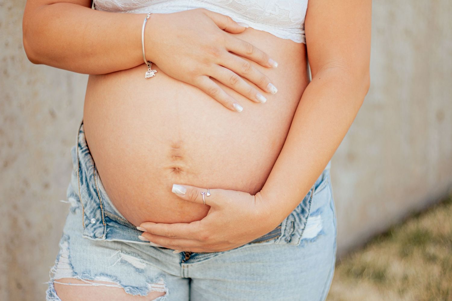 Close up view of a pregnant belly being cradled by hands while wearing light denim shorts.