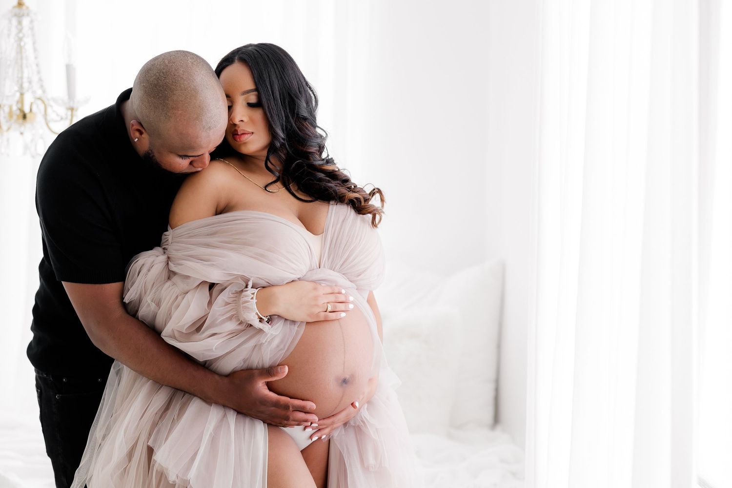 Tender maternity portrait featuring couple in intimate embrace against white background.