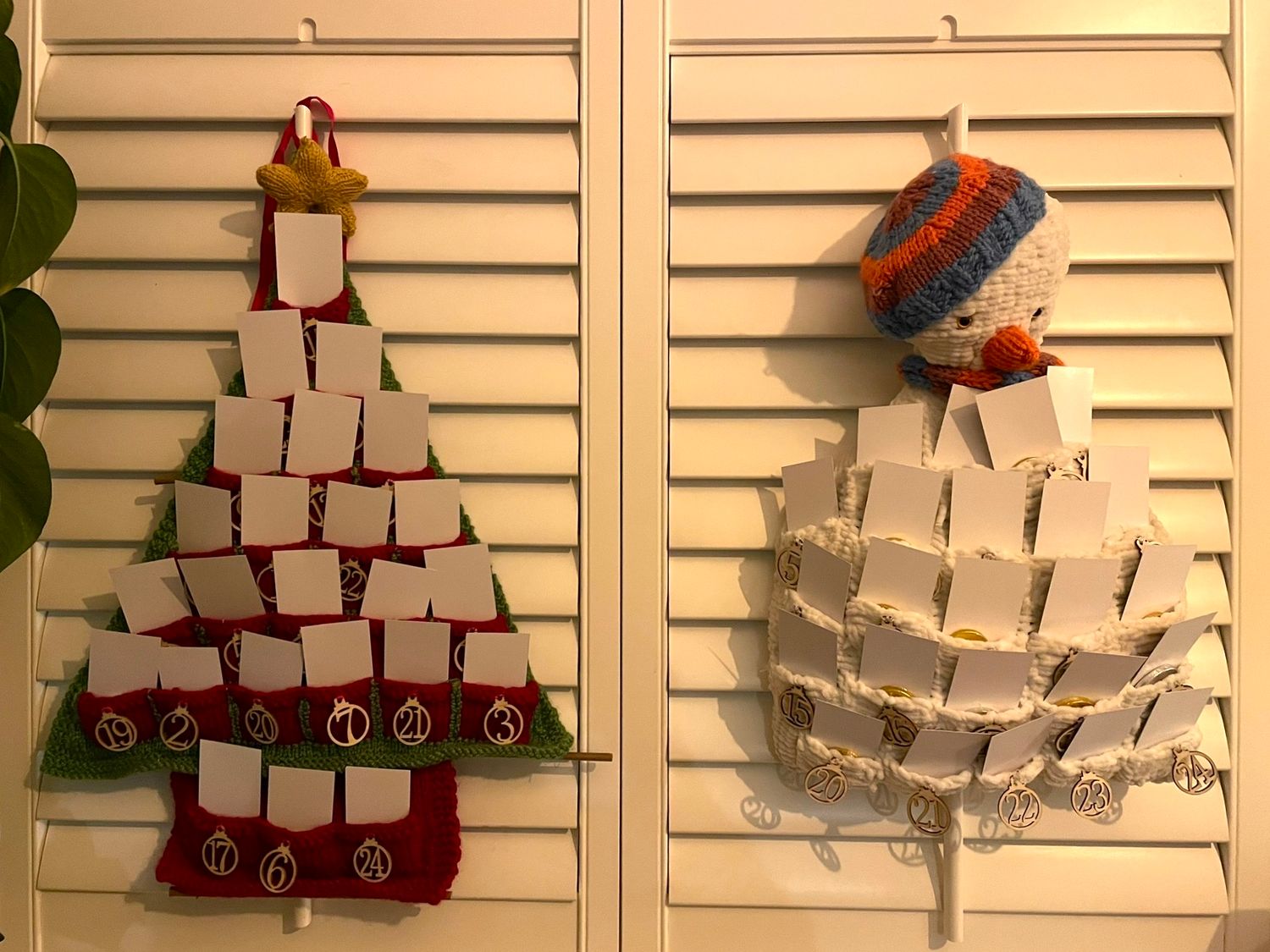 Two holiday advent calendars shaped like a Christmas tree and snowman made from paper boxes on shutters.