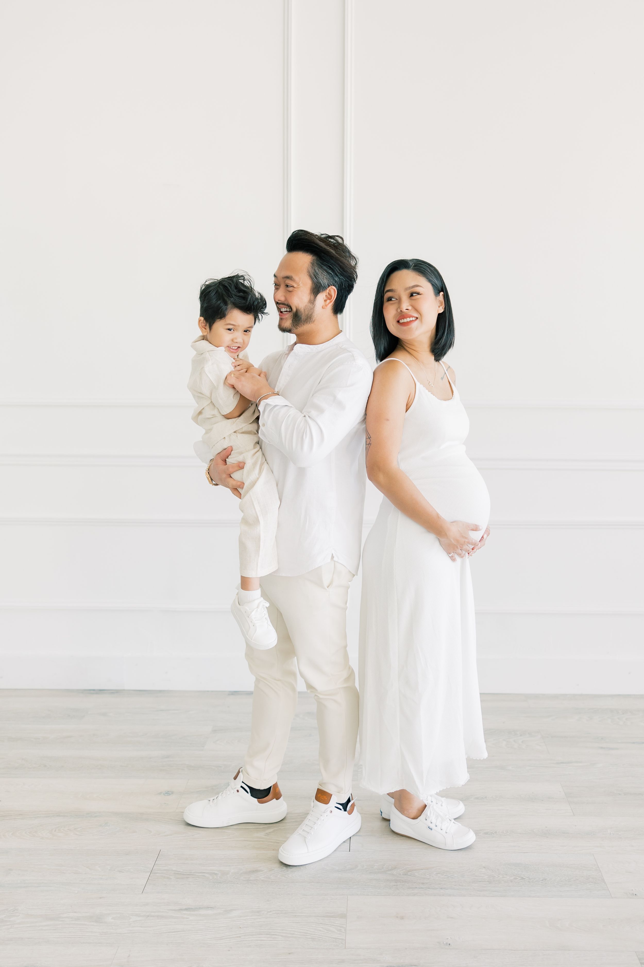 A family in all white outfits poses together against a minimalist white wall interior.