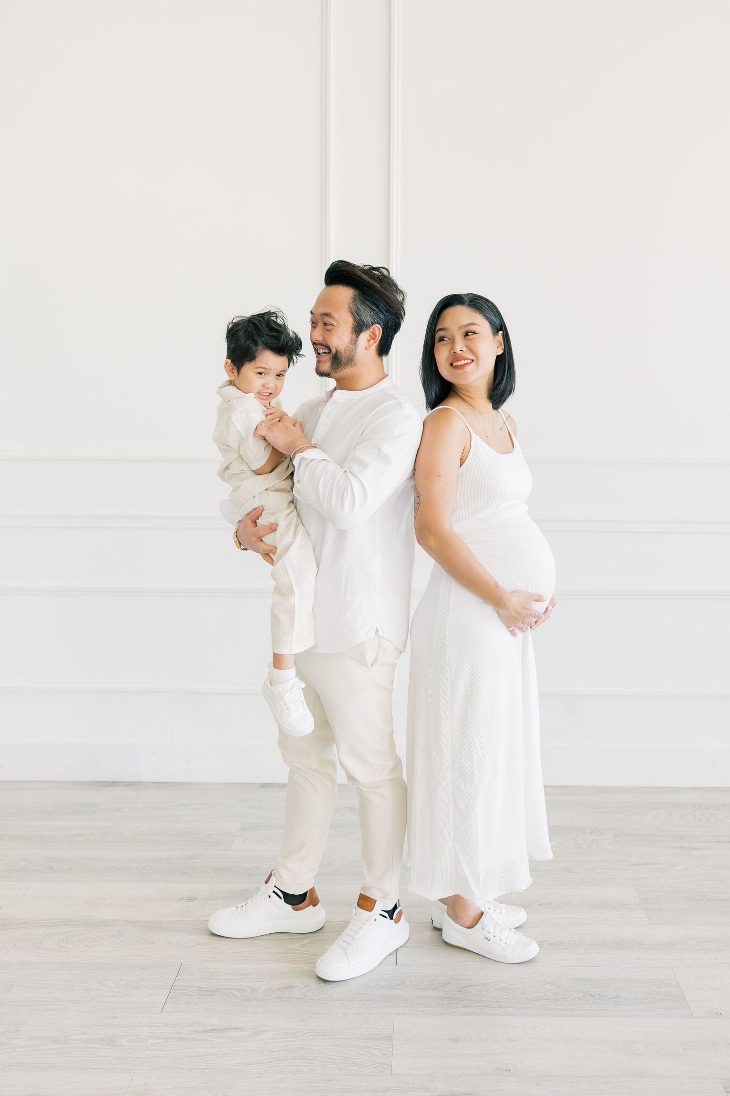 A family in all white outfits poses together against a minimalist white wall interior.