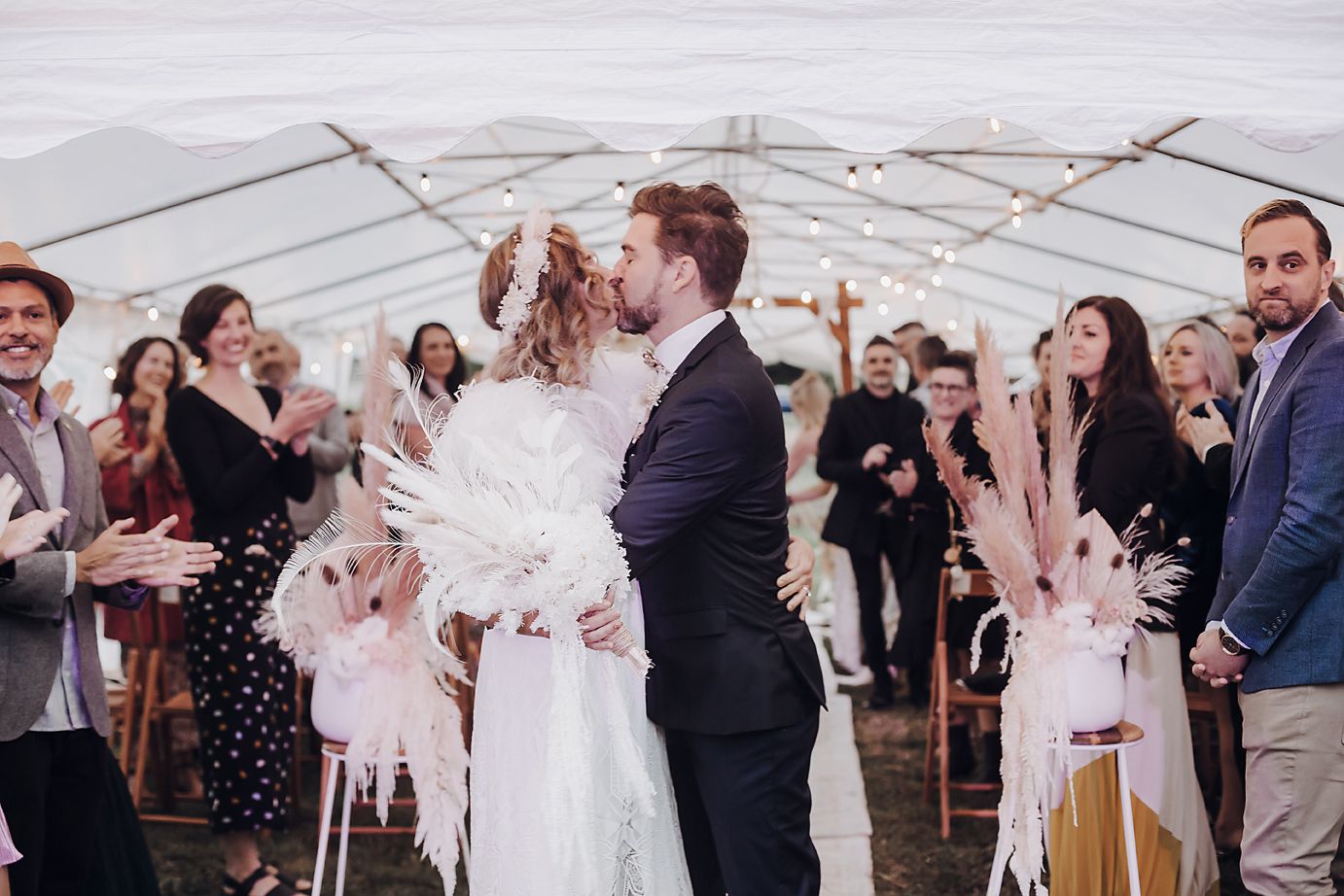 Wedding guests celebrate with sparklers and confetti under a white tent at outdoor reception.