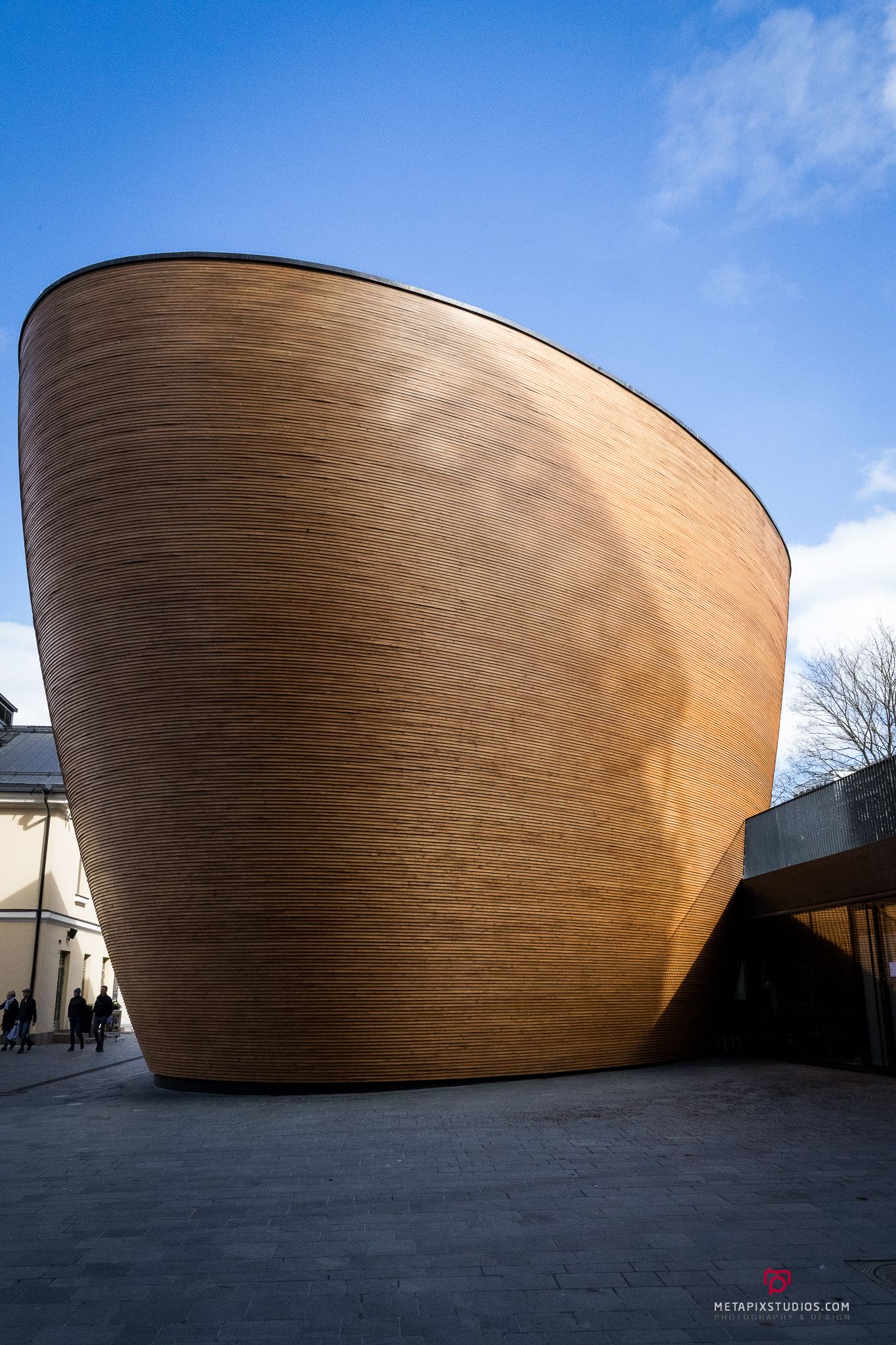Unique curved golden bronze architectural building with textured exterior surface against a bright blue sky in Helsinki.