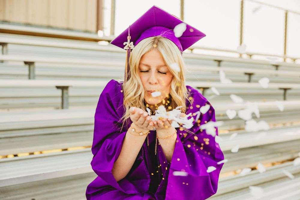 Graduate in purple gown celebrates with glitter confetti on outdoor bleachers.
