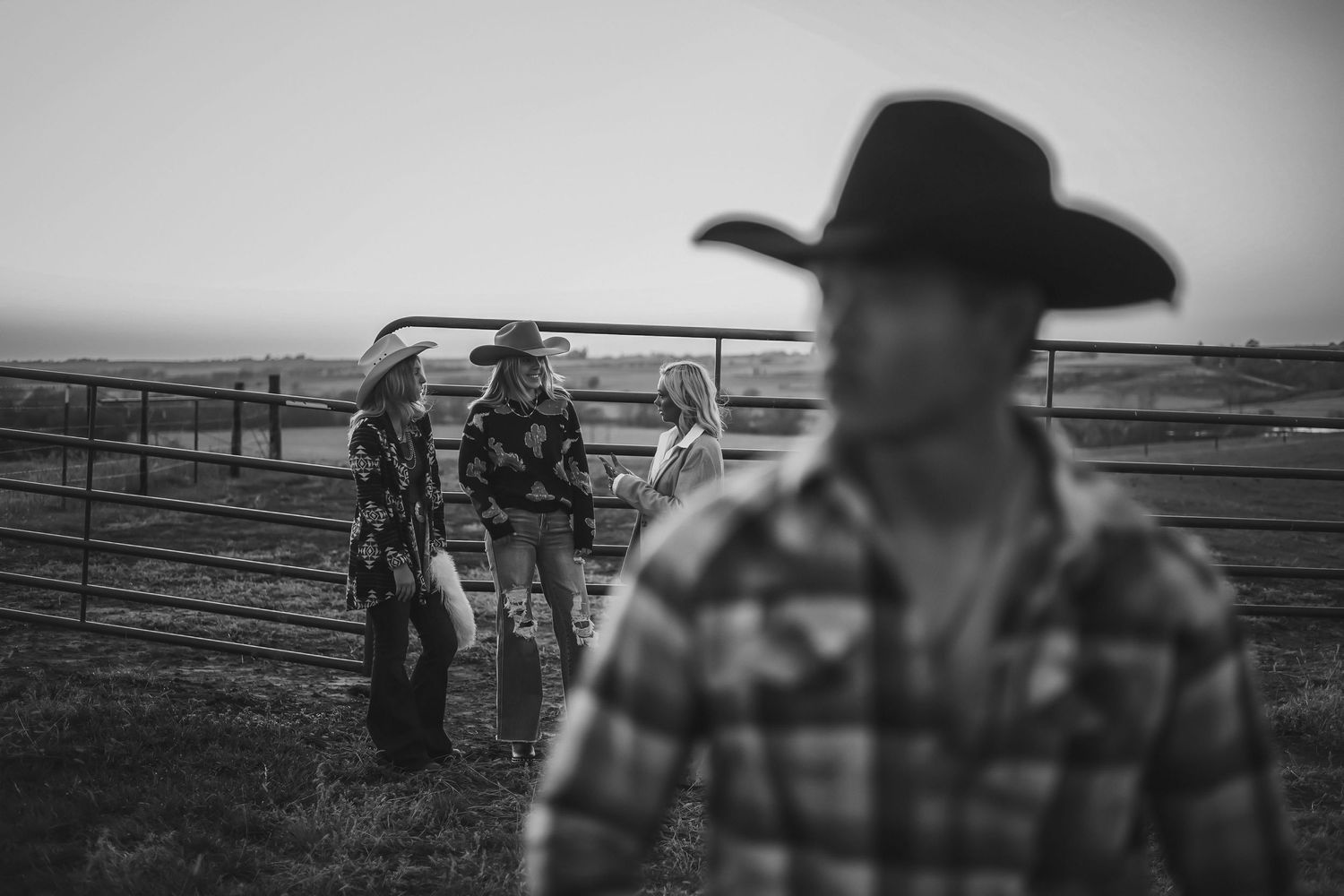 Black and white ranch scene with figures working near cattle pens at dusk.