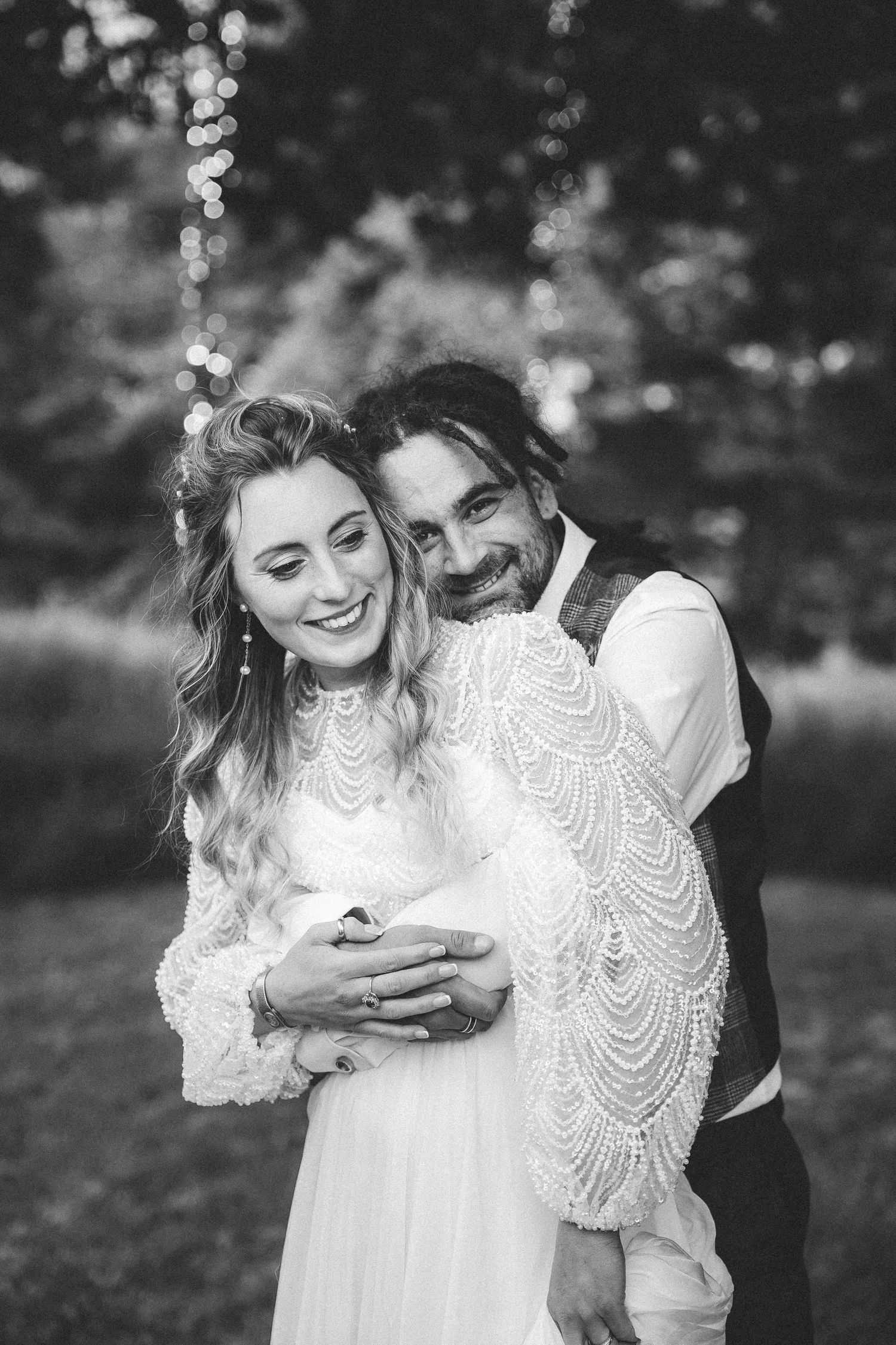 A couple shares a tender embrace while laughing together outdoors in black and white photography.