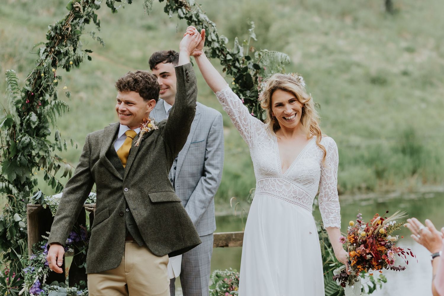 Bridal party wearing sage green dresses walk together through a scenic hillside meadow on an overcast day.