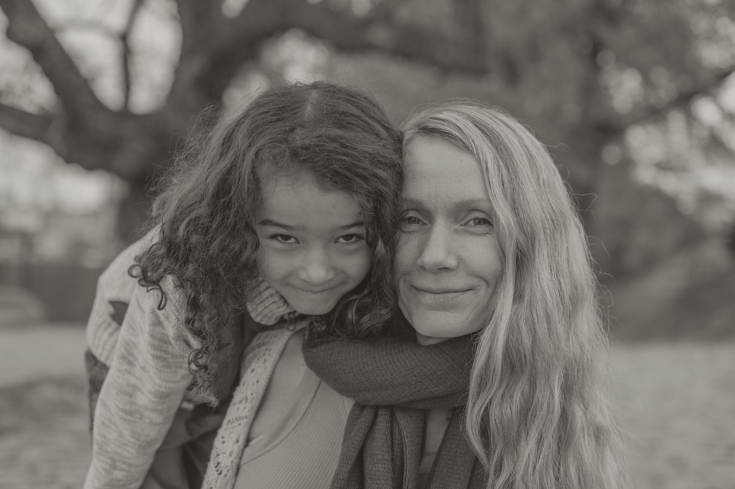 A black and white portrait of two people hugging and smiling warmly outdoors on a winter day.