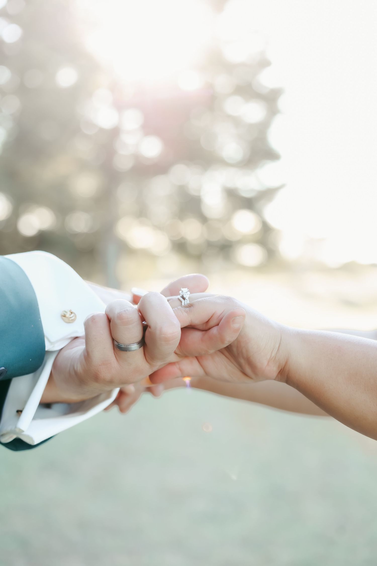 Close-up of hands with engagement ring against bokeh background outdoors.