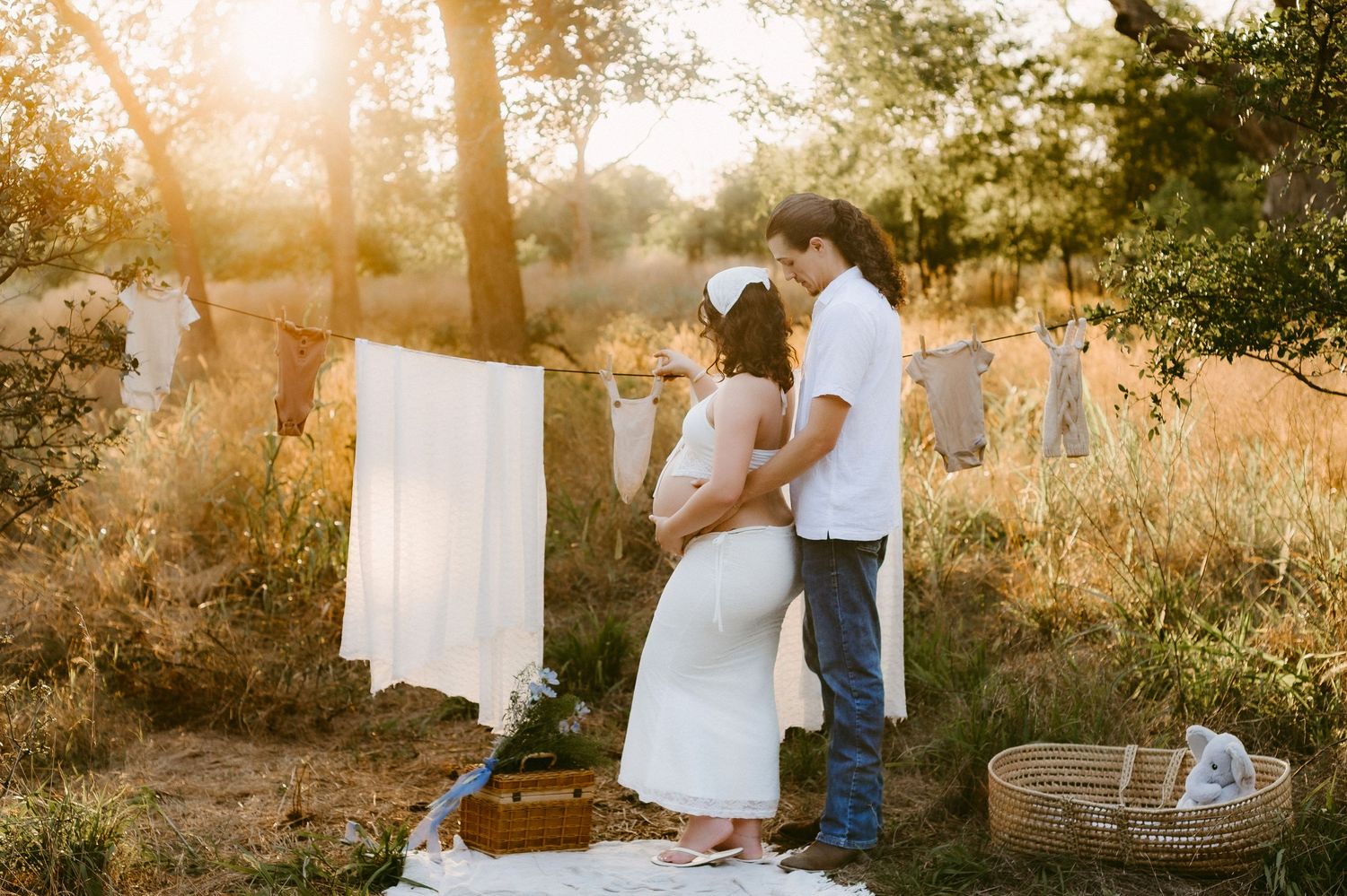 A maternity photo session in a sun-drenched field with white fabric hanging from trees.