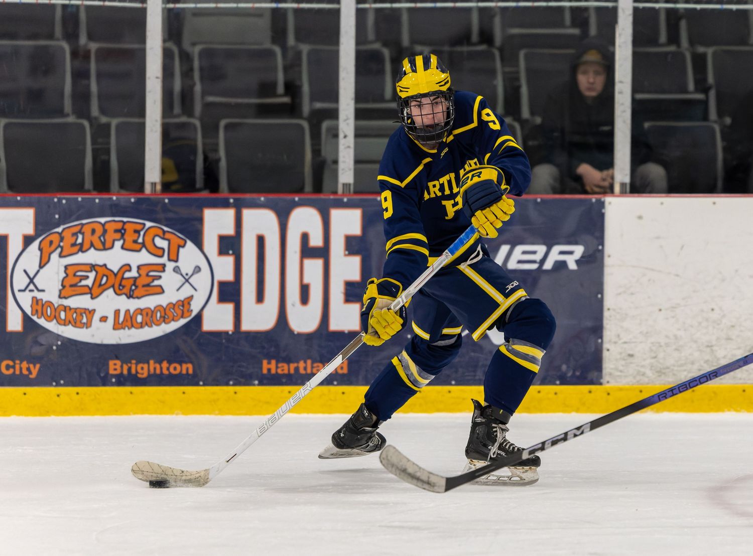 Ice hockey players in yellow and blue jerseys compete during a game on the rink with visible hockey equipment.