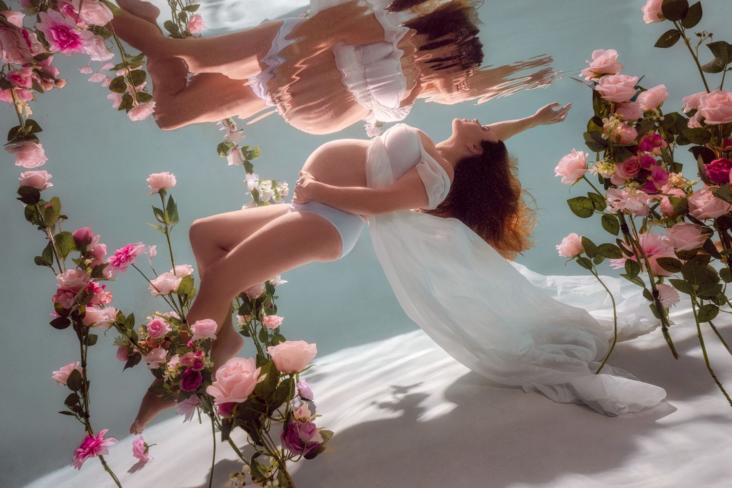 Ethereal underwater scene with flowing white fabric and pink roses creating a dreamy, artistic composition.