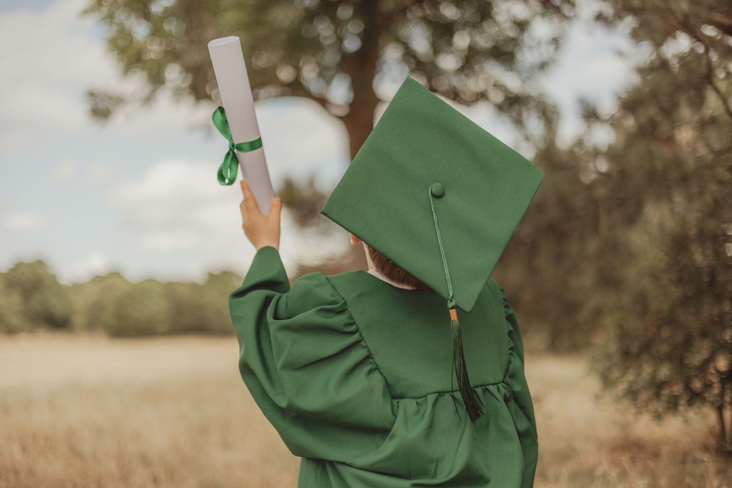 Person in green graduation gown celebrating outdoors.