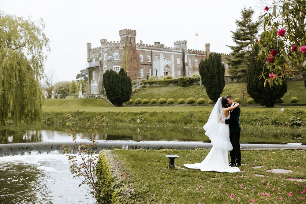 Romantic wedding couple poses in elegant garden setting with castle and lake. Bellingham Castle Conlon Photo & Film